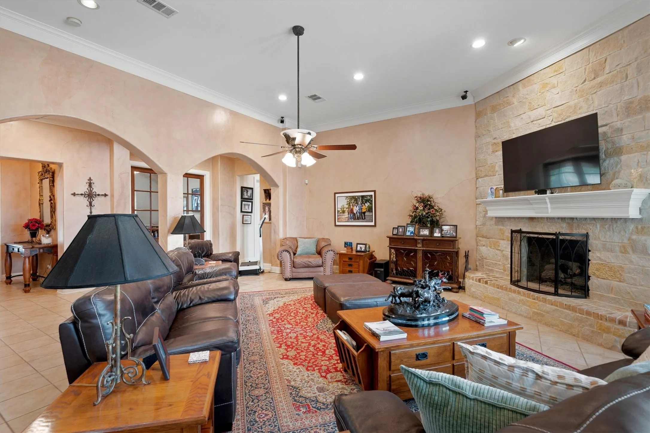 Living area featuring a stone-clad fireplace with a white mantel, recessed lighting, crown molding, and arched doorways