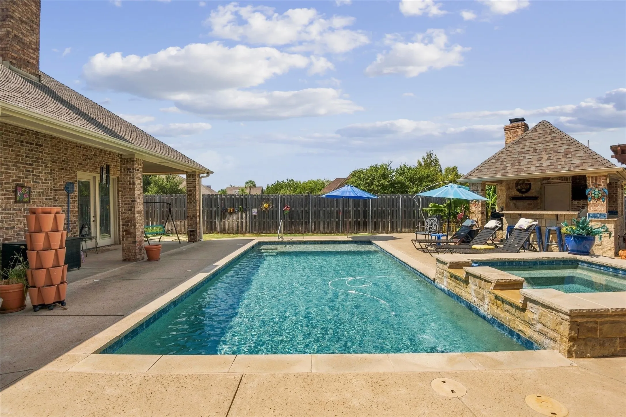 Rectangular swimming pool with integrated spa, expansive concrete patio, covered outdoor living area, brick exterior, and a dedicated outdoor kitchen structure