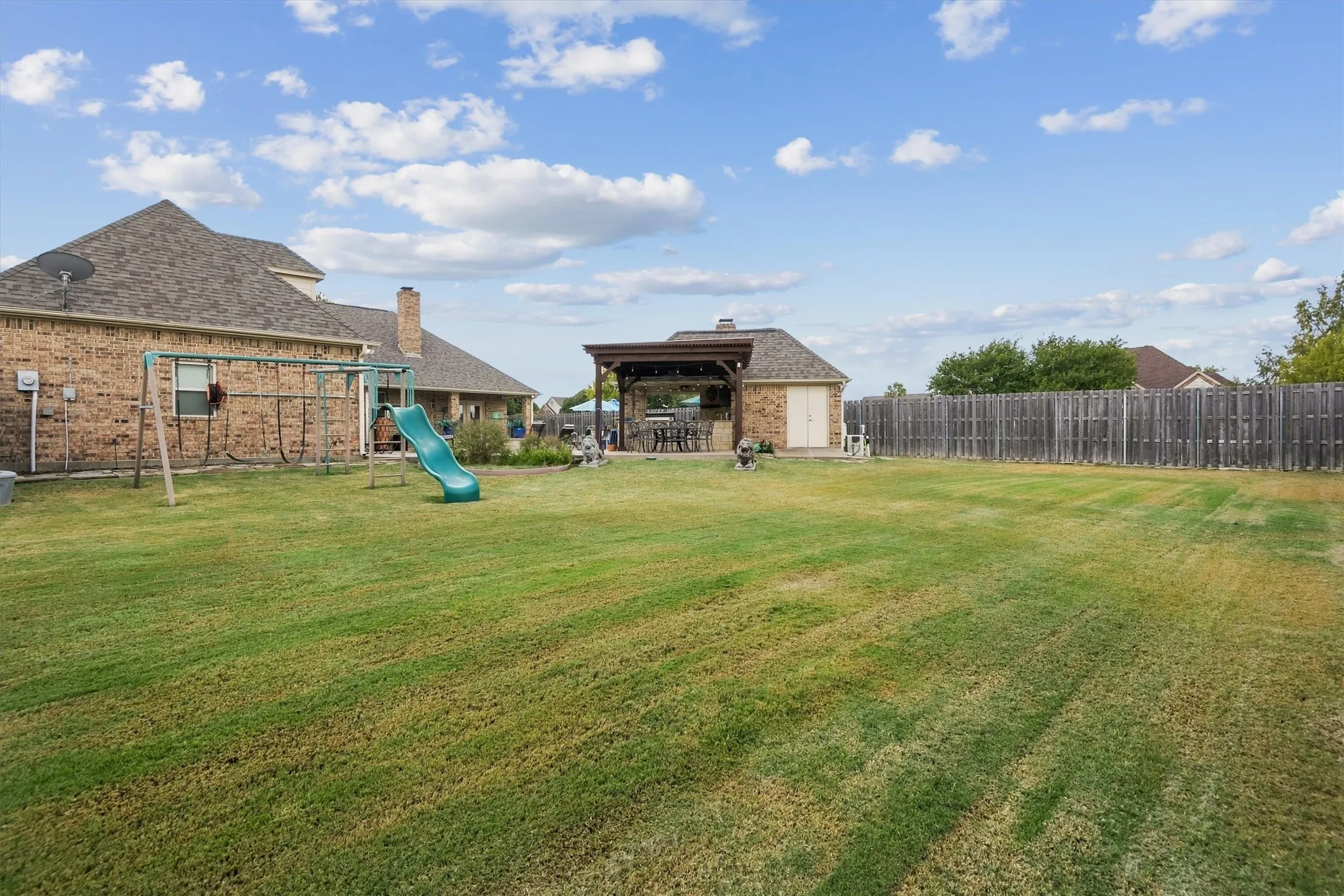 Expansive backyard featuring a brick exterior, wood fence, and a pergola-covered patio
