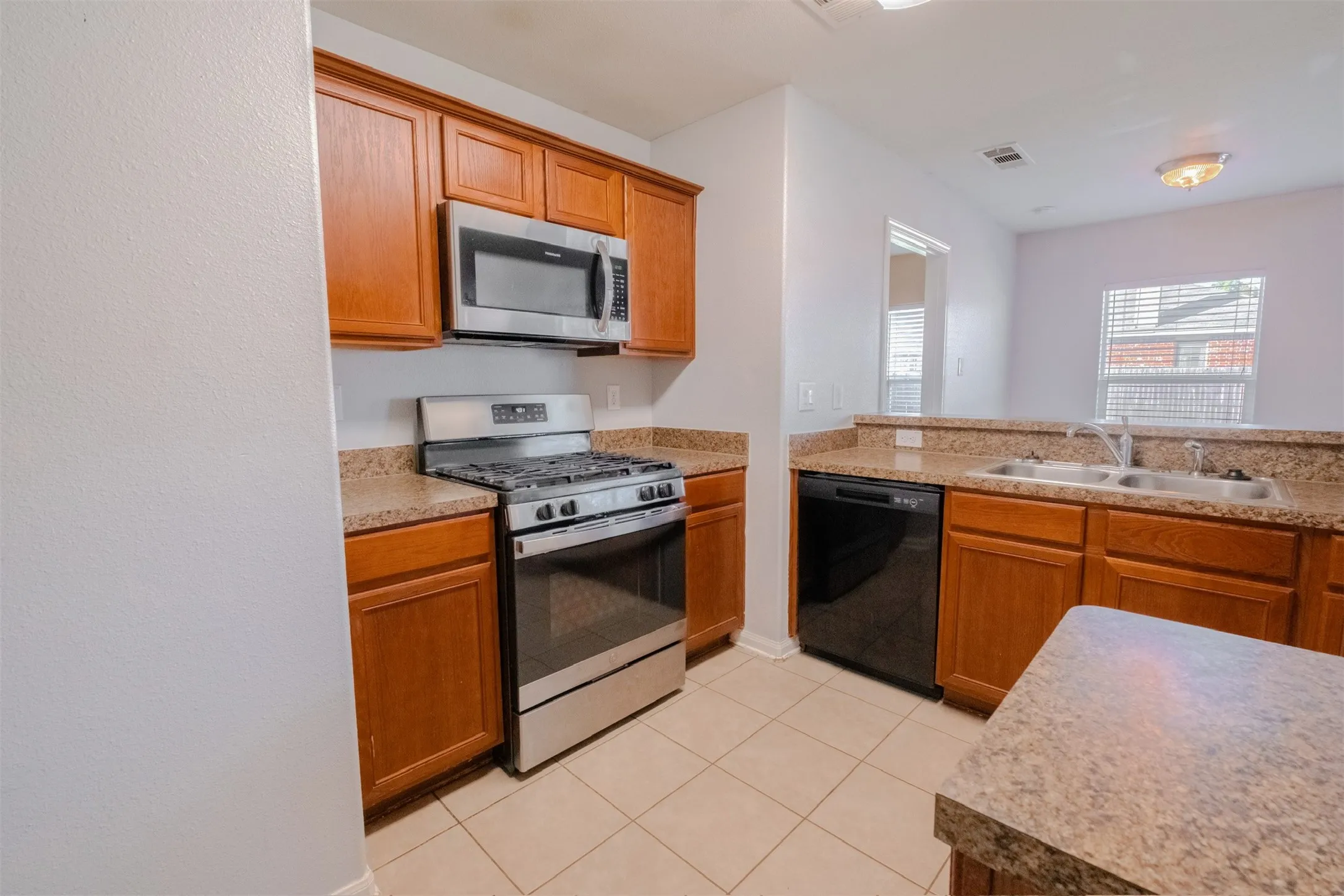 Kitchen with stainless steel appliances, light tile patterned flooring, light countertops, and brown cabinetry