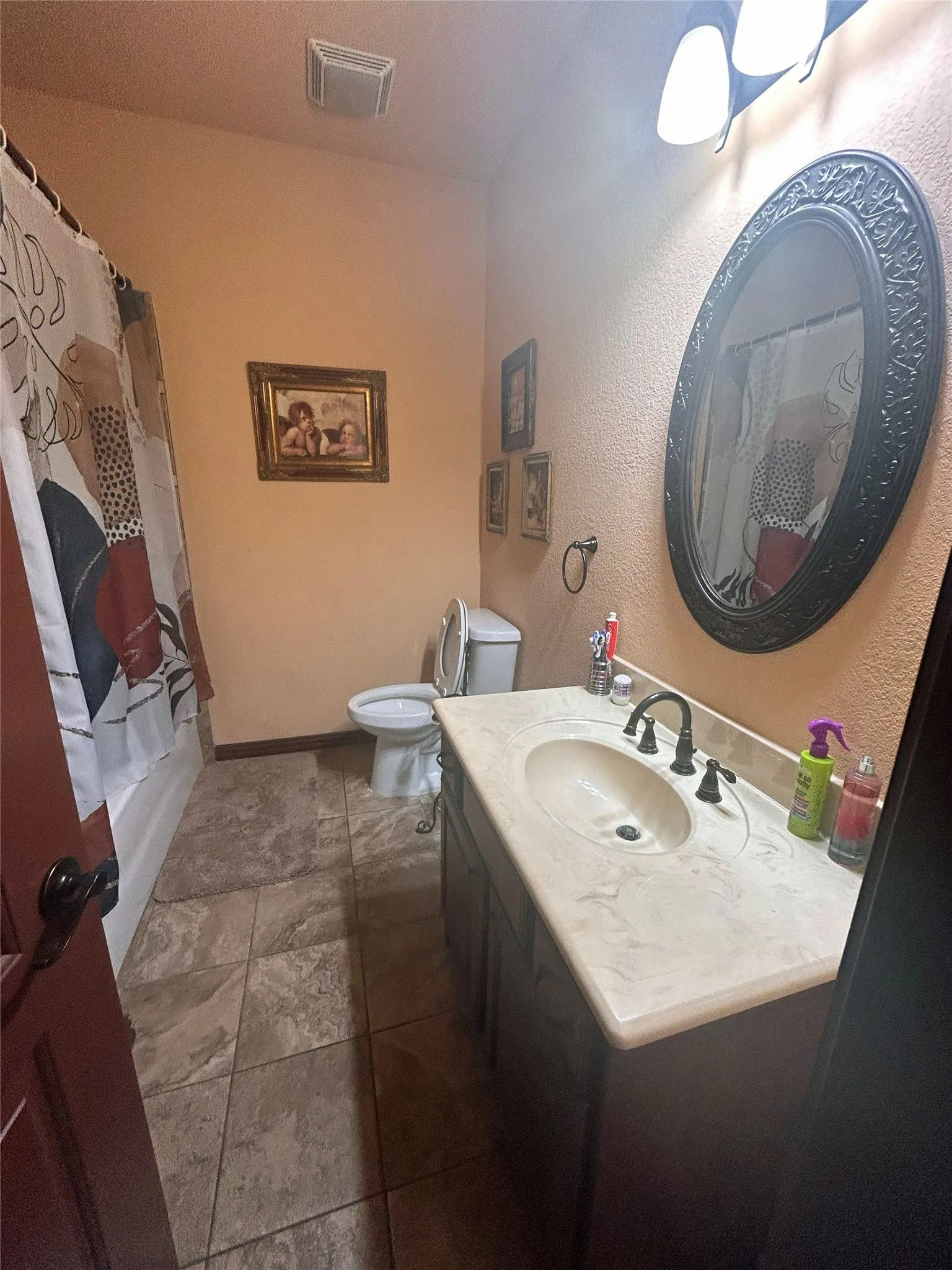 Vanity with integrated sink, dark cabinetry, decorative framed mirror, and tiled flooring