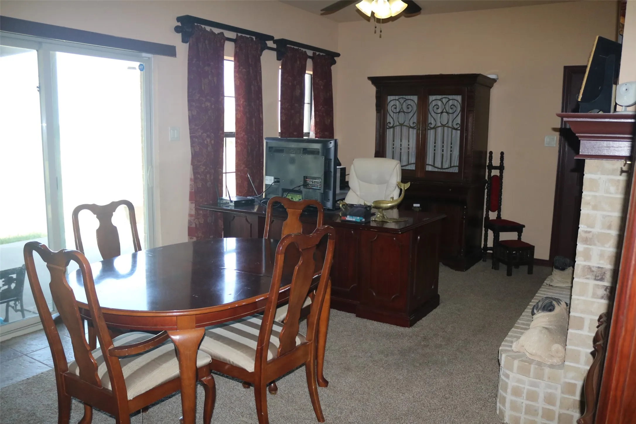 Sliding glass door, overhead ceiling fan, carpeted flooring, brick-faced fireplace, and window with rod and drapes