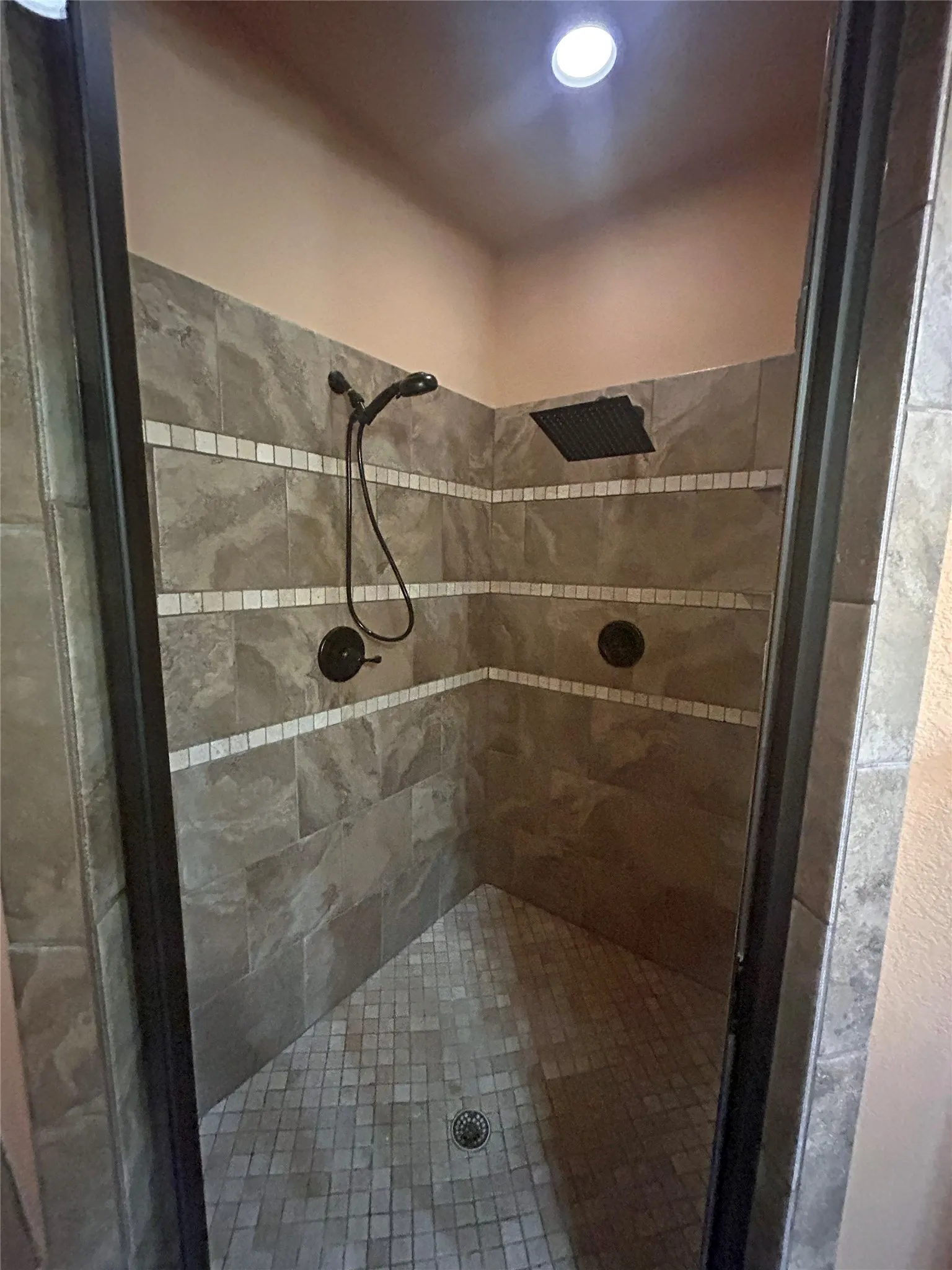 Tiled shower enclosure featuring a fixed showerhead, handheld sprayer, and rain showerhead