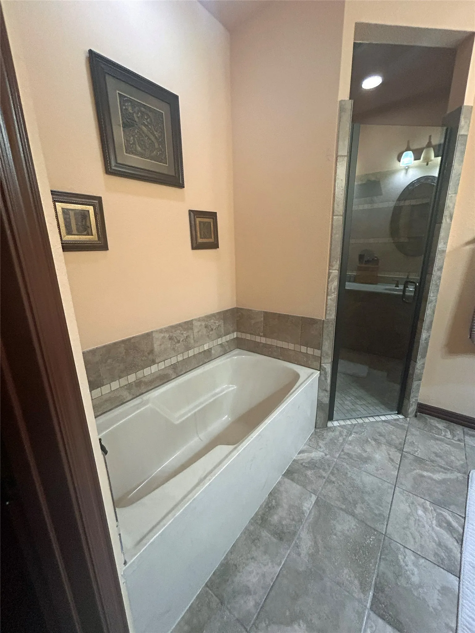Bathtub with tiled surround, separate shower with glass enclosure, and large format floor tiling