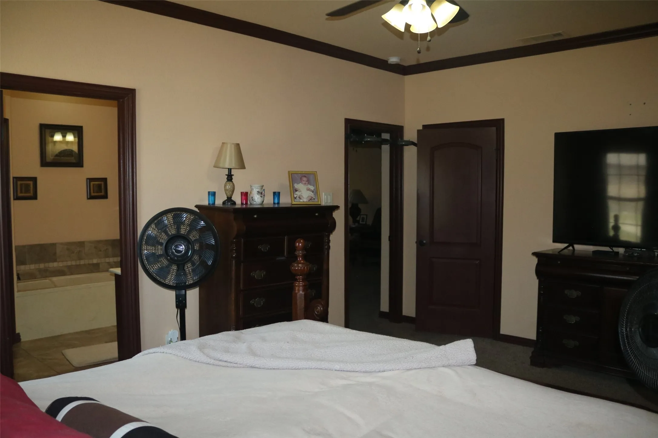 Ceiling fan light fixture, dark wood-finish trim, interior paneled door, built-in soaking tub with stone tile surround, and tile flooring in the adjacent bathroom