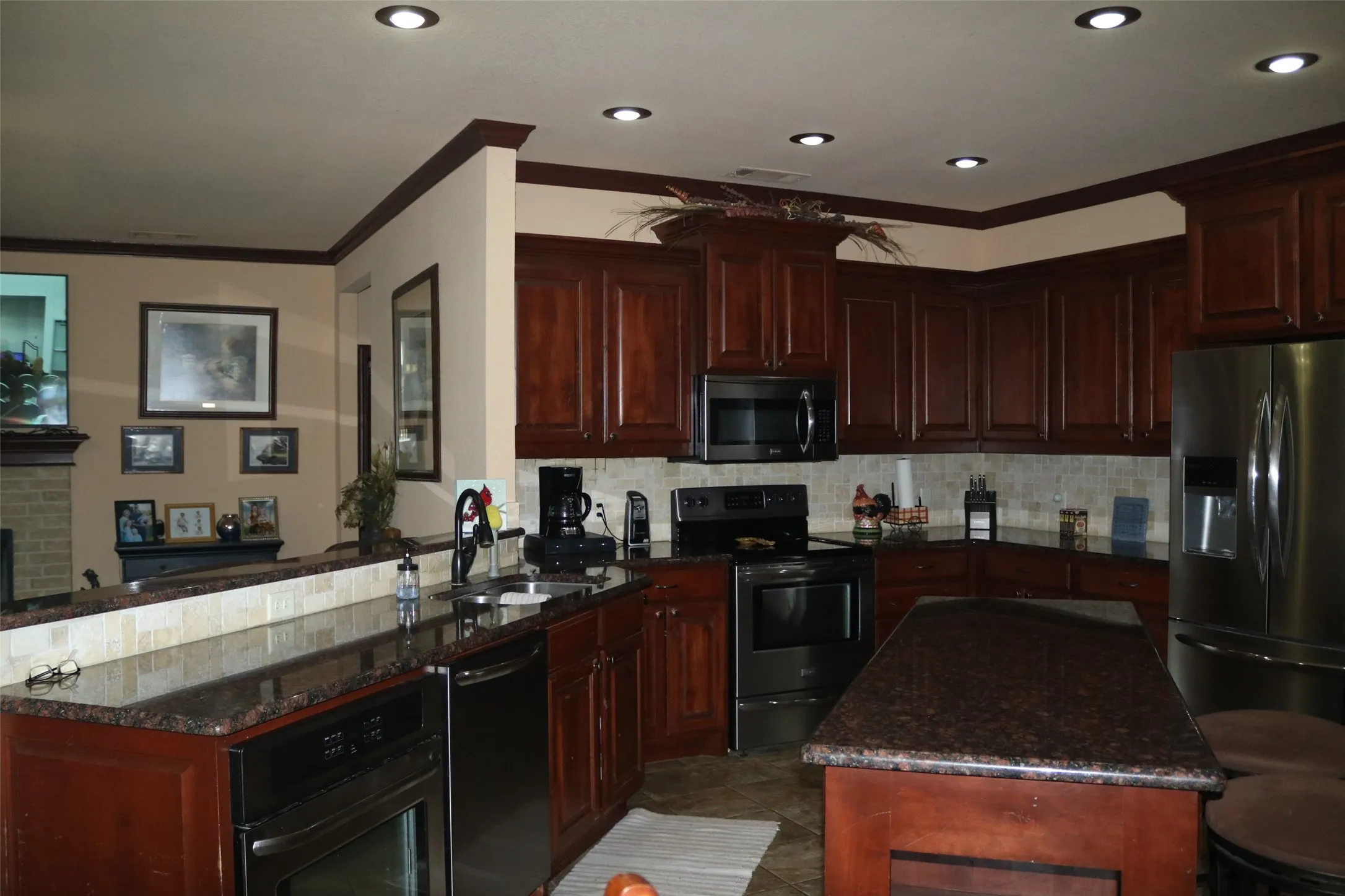 Kitchen featuring dark wood cabinetry, granite countertops, stainless steel appliances, a tiled backsplash, and recessed lighting
