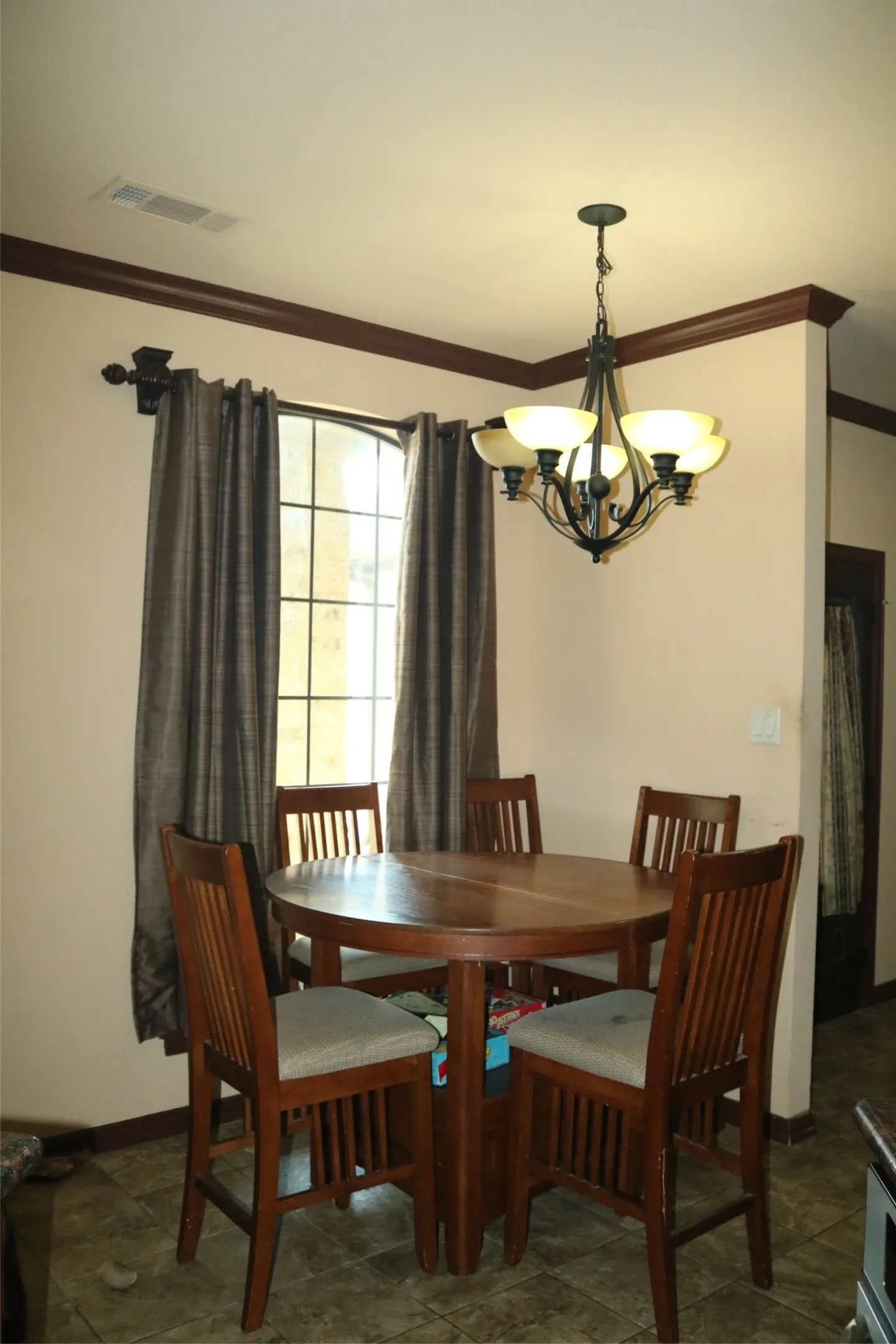Arch-top window with grid pattern, overhead chandelier with frosted glass shades, crown molding, and tiled flooring