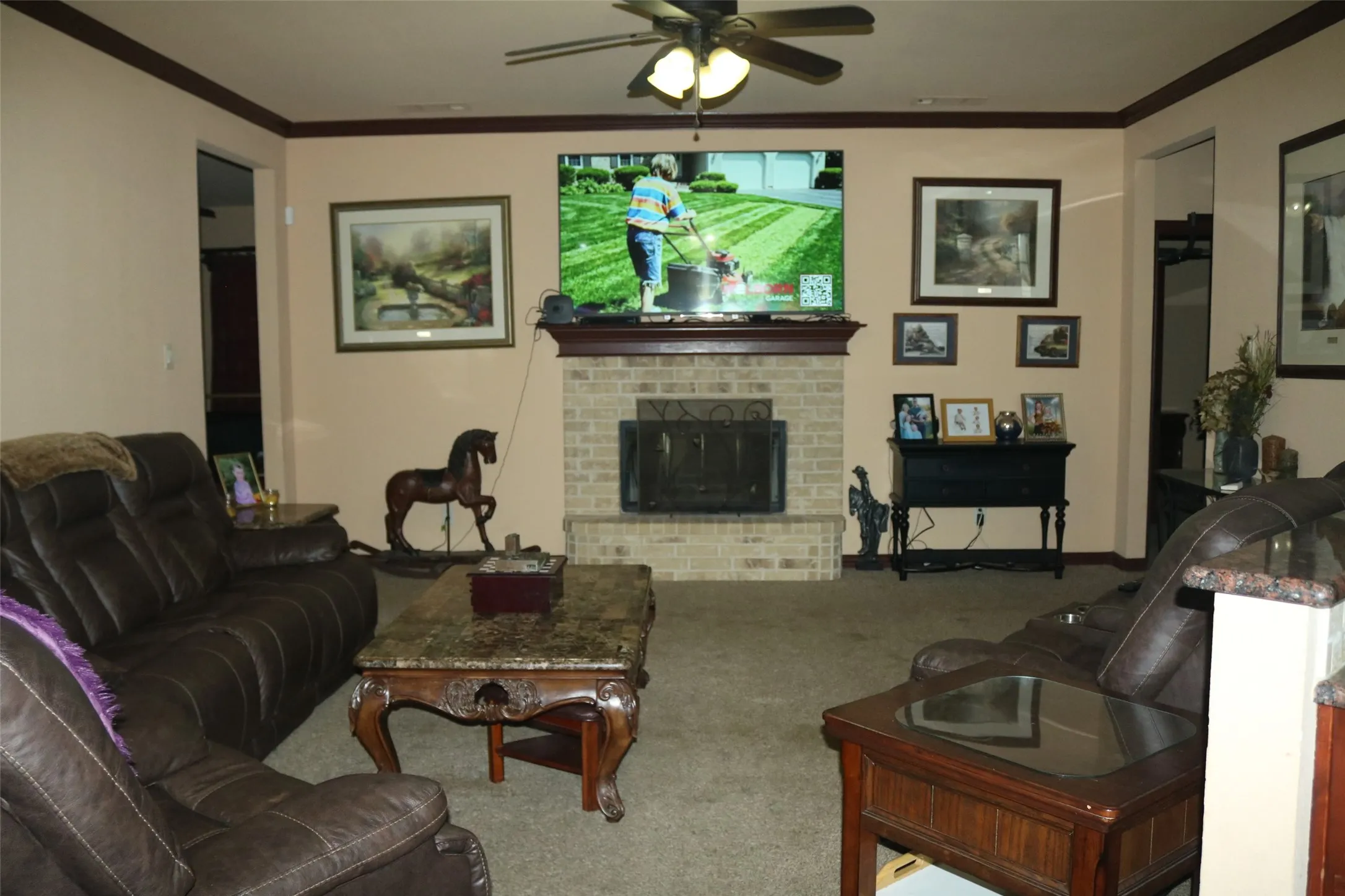 Brick-surround fireplace with a dark wood mantel and hearth, tray ceiling, and a ceiling fan with integrated lighting