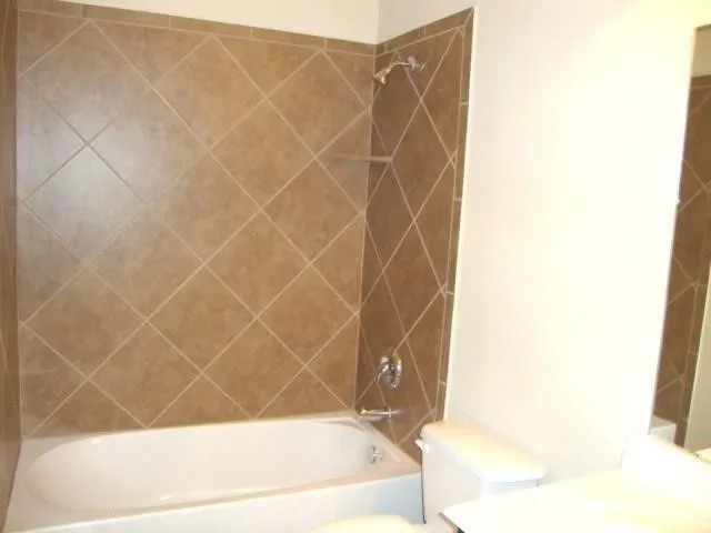 Bathtub and shower combination featuring diamond-patterned wall tile, chrome fixtures, and an integrated shelf