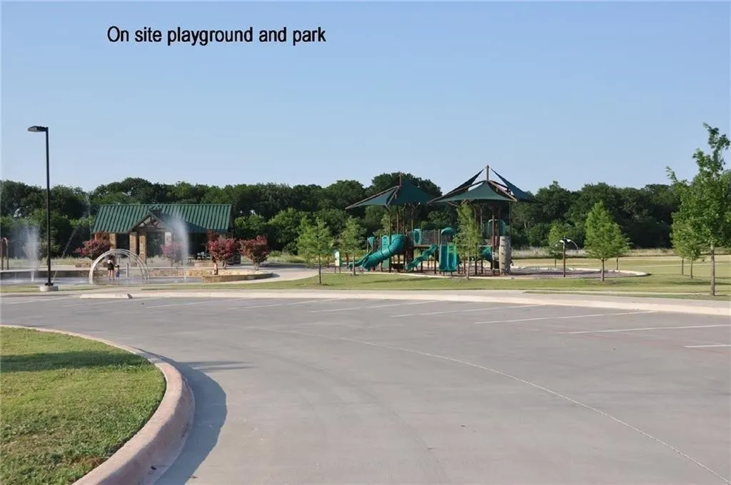 Community park featuring a splash pad, playground structures with sun shades, green space, and mature trees