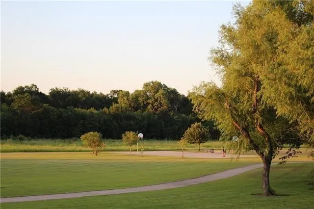 Expansive green space featuring a paved pathway, mature trees, and a basketball hoop