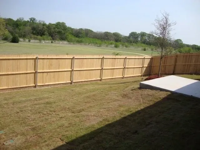 Wood privacy fencing enclosing a grassy yard with a concrete patio pad