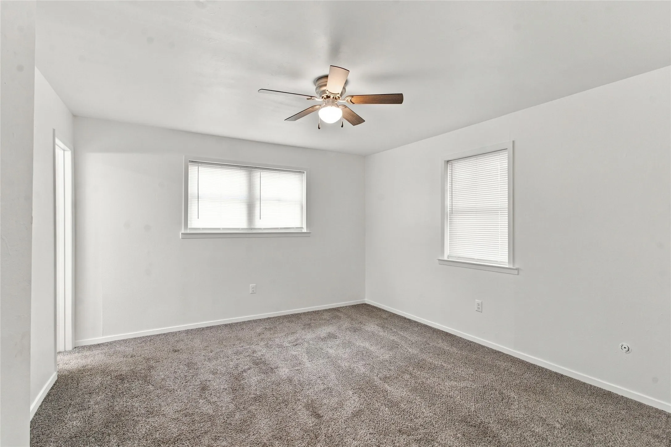 Neutral carpet flooring, white painted walls, and a ceiling fan with integrated lighting