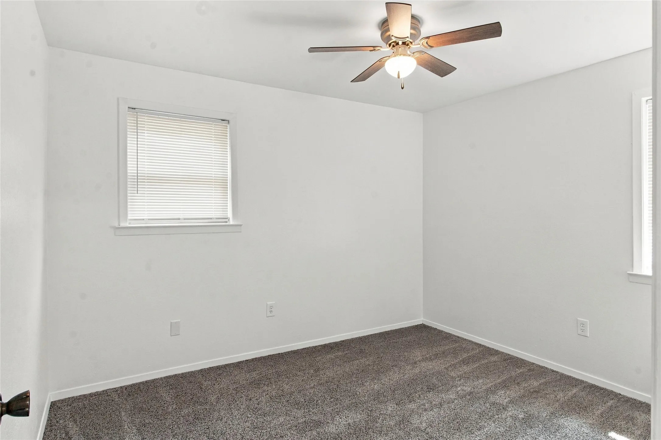 Wall-to-wall carpeting, ceiling fan with light fixture, and two windows with blinds