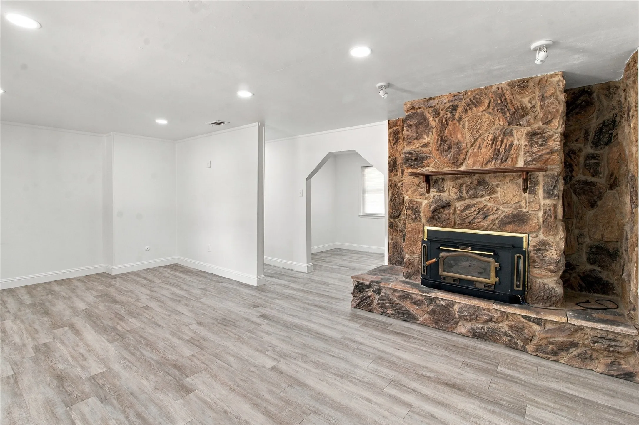 Expansive living area with wood-finish flooring, recessed lighting, and a stone-clad fireplace with a wood mantel