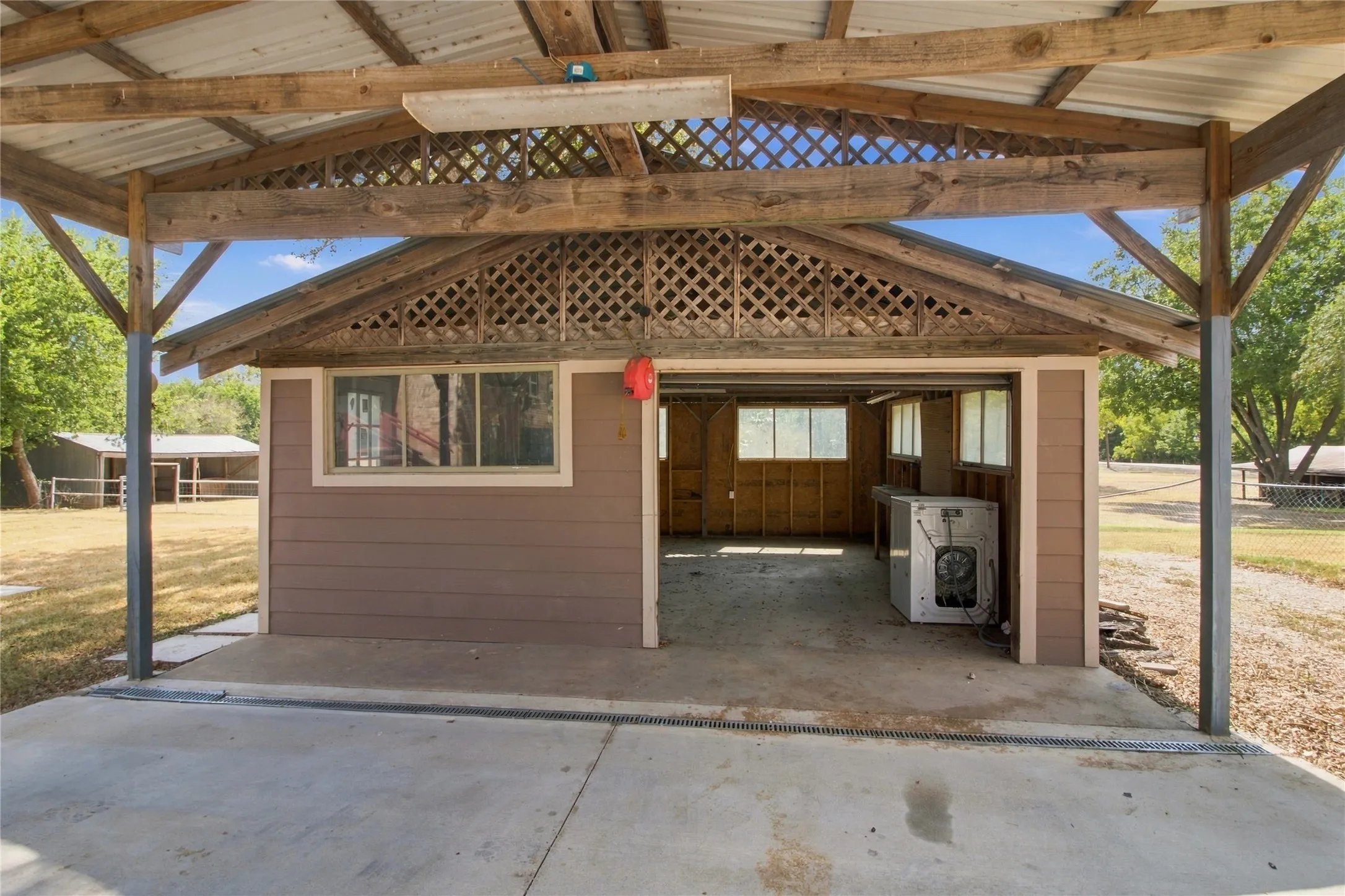 Covered outdoor space featuring a concrete pad, metal roof, and exposed wood beams