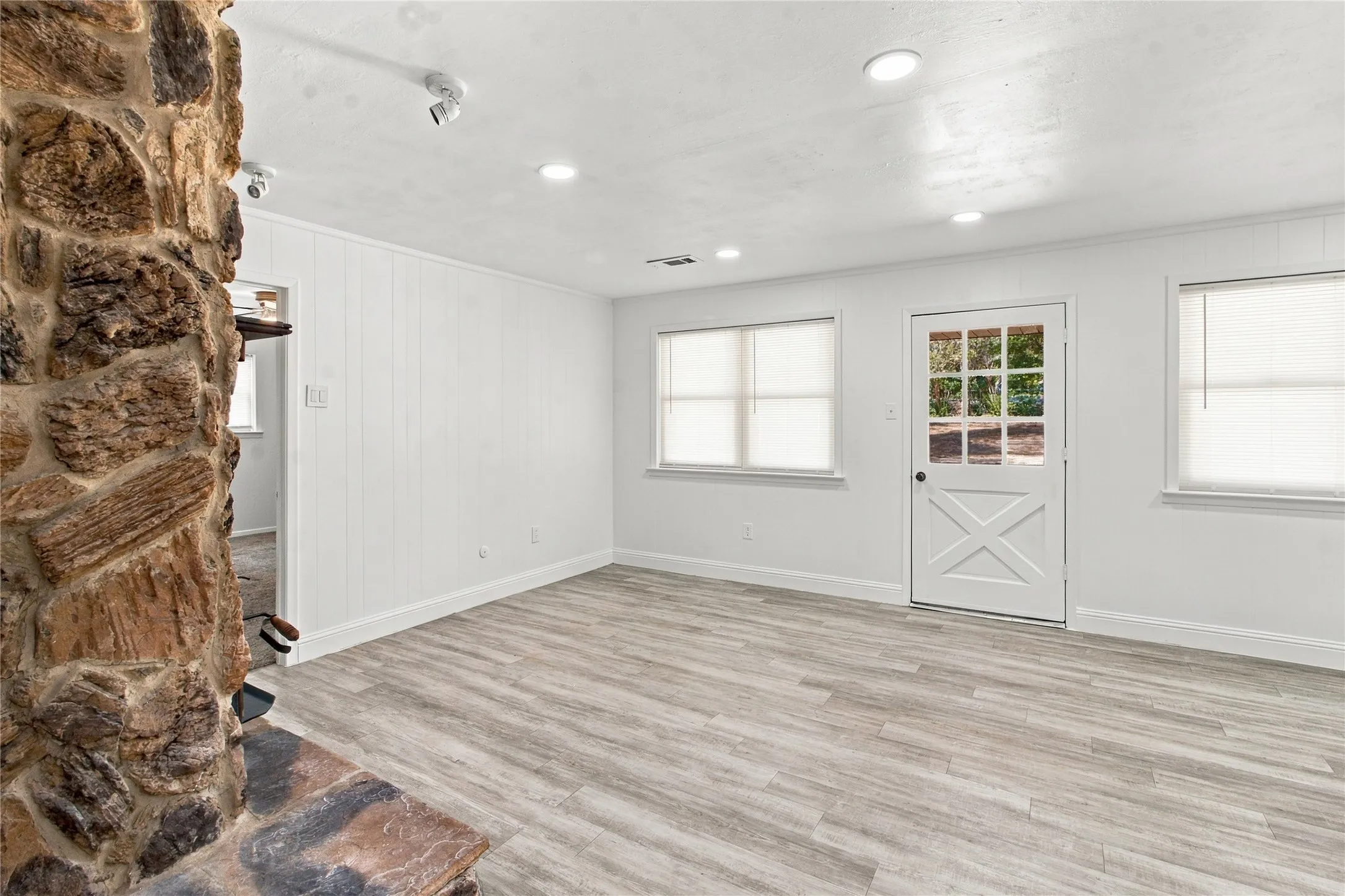 Stone-clad fireplace with a hearth, wood-finish flooring, white paneled walls, recessed lighting, and a door with divided lites