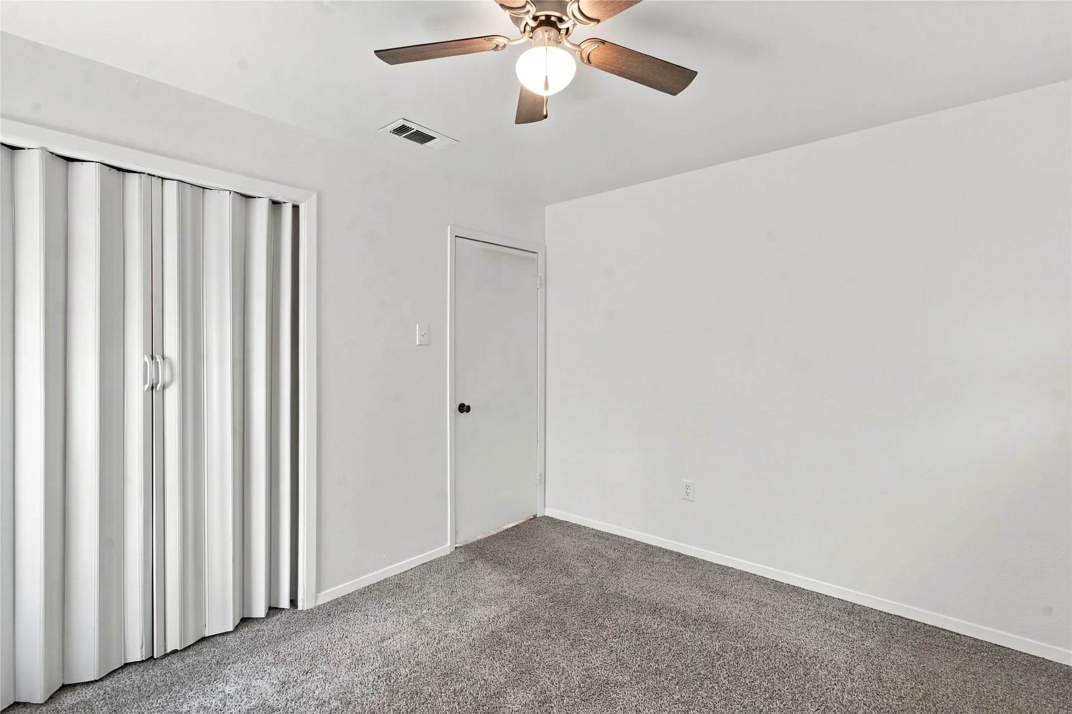 Neutral wall finishes, textured carpeting, accordion closet doors, and overhead lighting with a ceiling fan