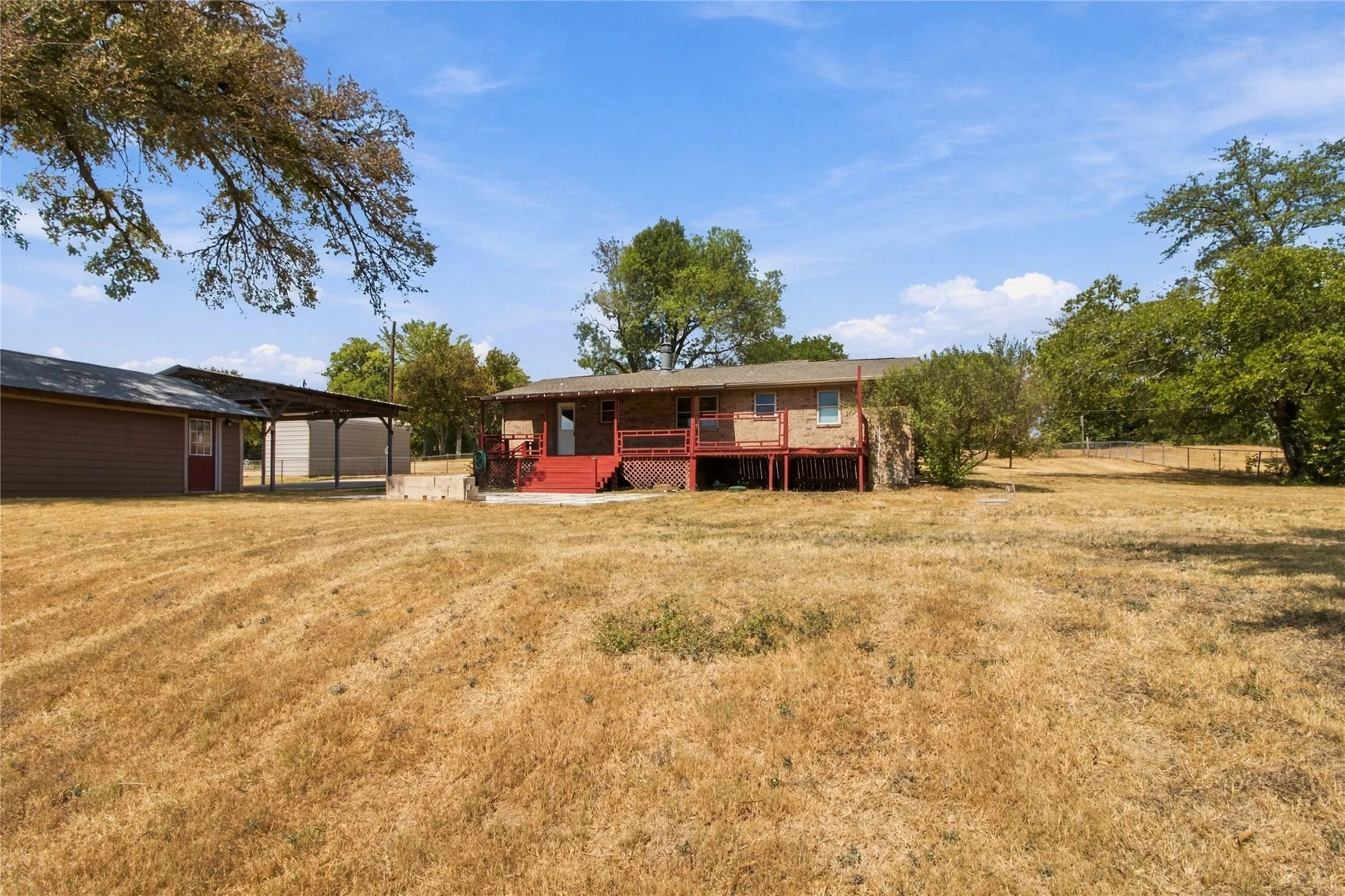Expansive outdoor area featuring a detached structure, a carport, and a raised exterior deck