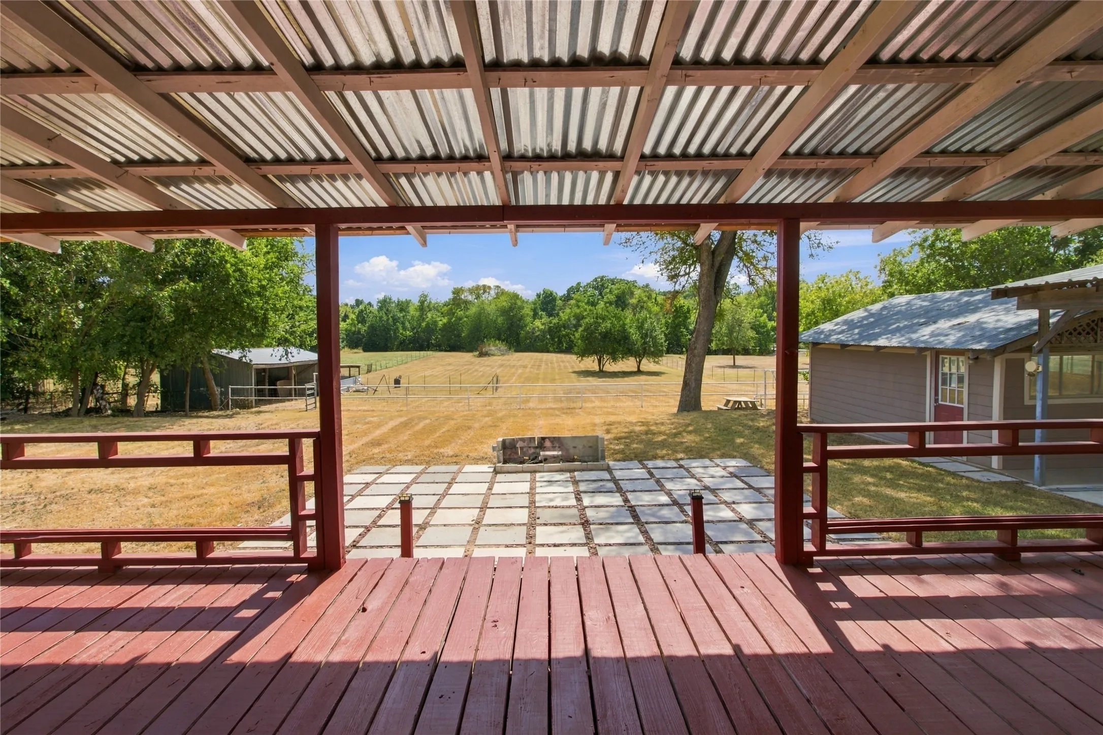 Expansive wood deck with a corrugated metal roof, leading to a large outdoor patio area with concrete pavers and a fire pit