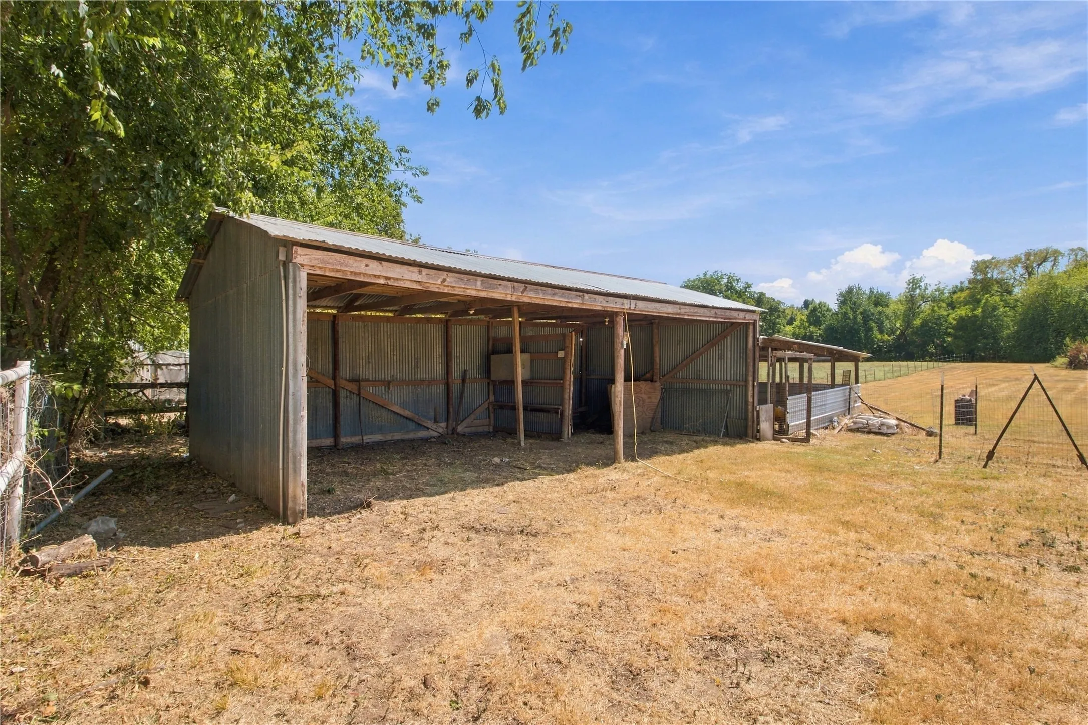 Corrugated metal outbuilding with a partially open front, timber frame construction, and a gabled roofline