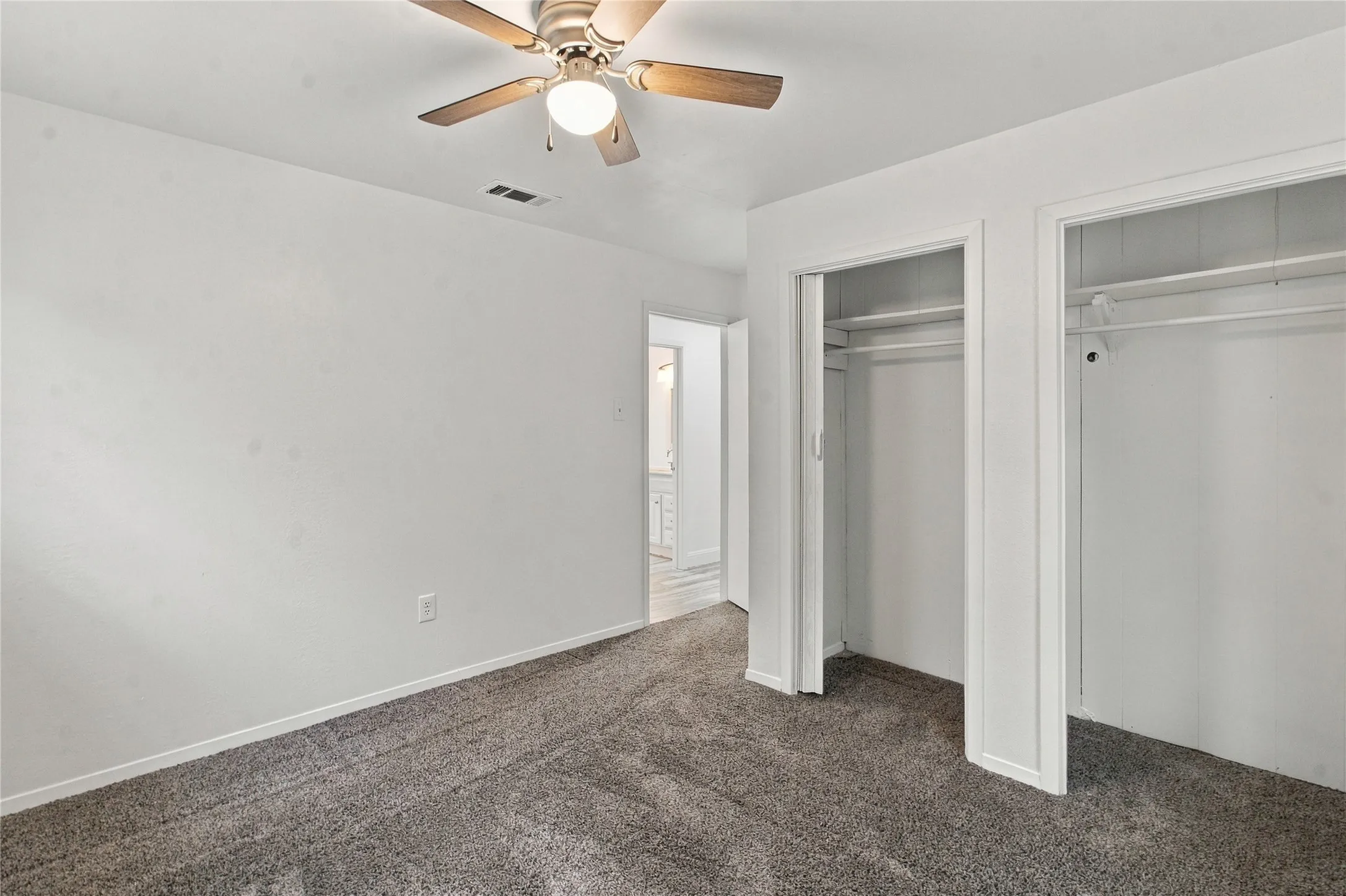 Plush gray carpeting, white painted walls, and a ceiling fan with light fixture