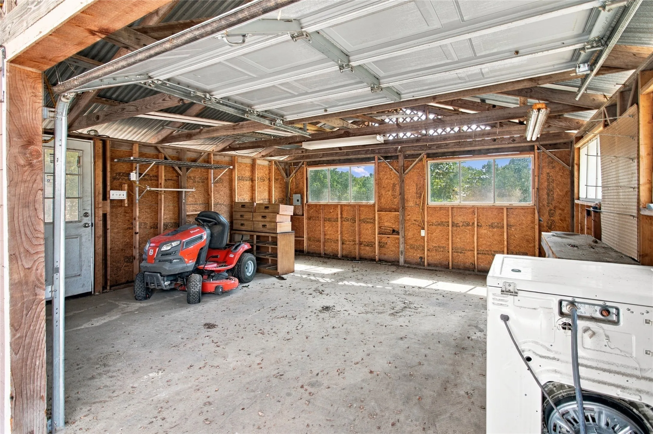 Concrete flooring, exposed wood beam ceiling, multiple windows, interior access door, corrugated metal roofing