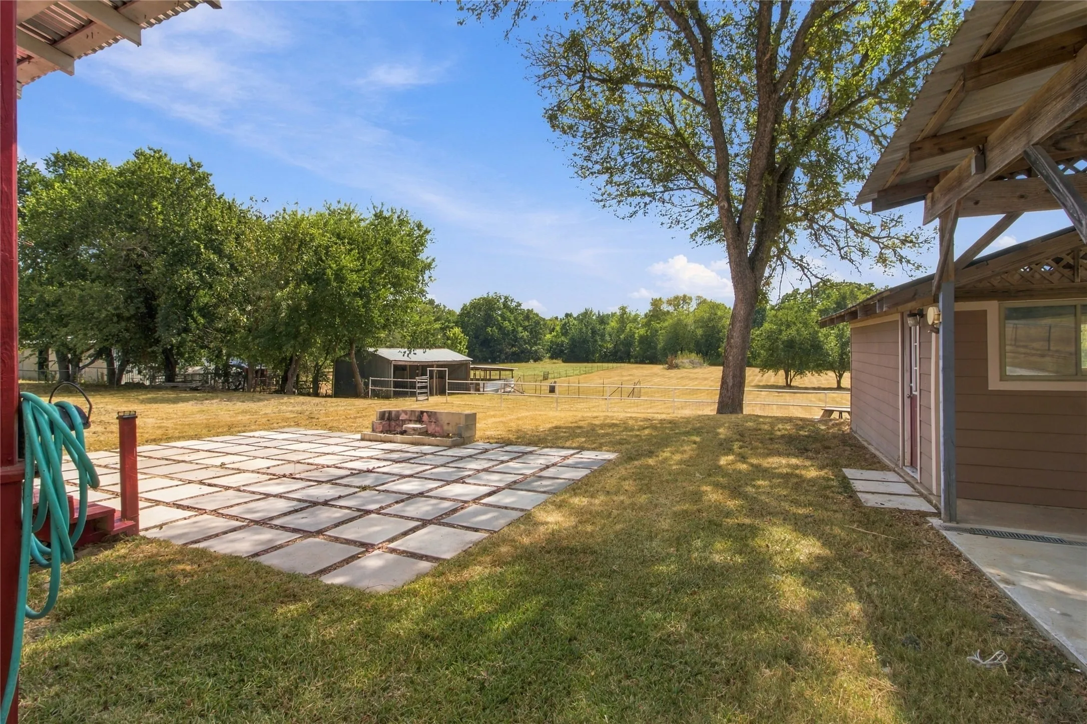 Expansive property featuring a paved patio area, an outdoor fire pit, and a separate utility building, all surrounded by mature trees