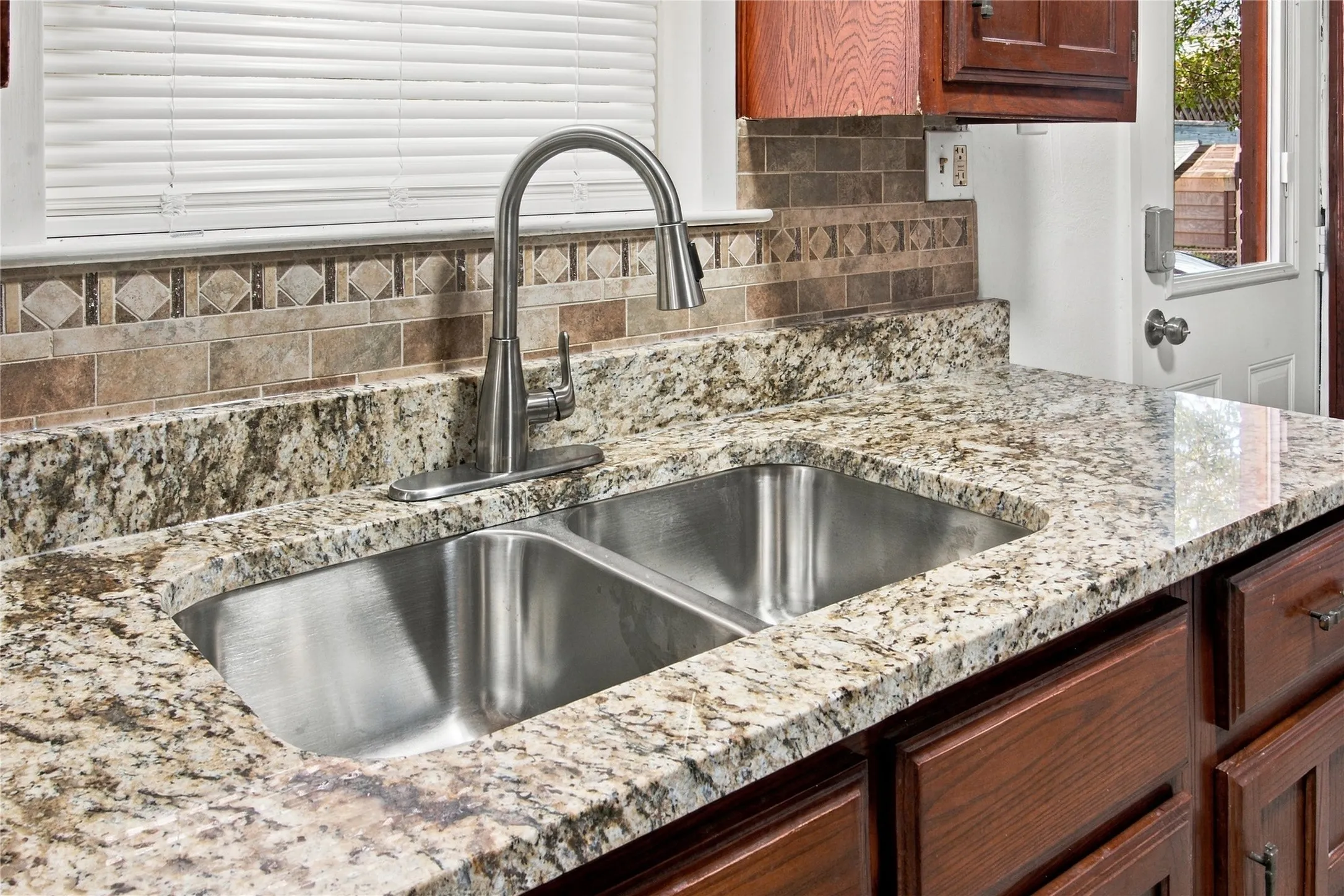 Dual-basin stainless steel sink with a high-arch faucet, set into a speckled countertop