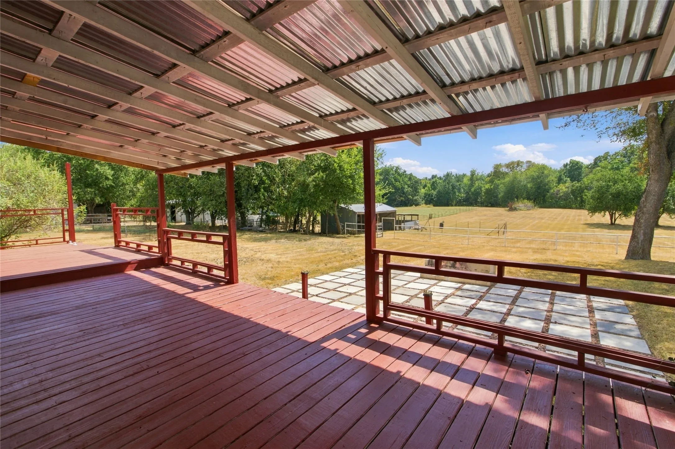 Expansive covered deck with red-stained wood flooring and metal railings, featuring a galvanized metal roof structure