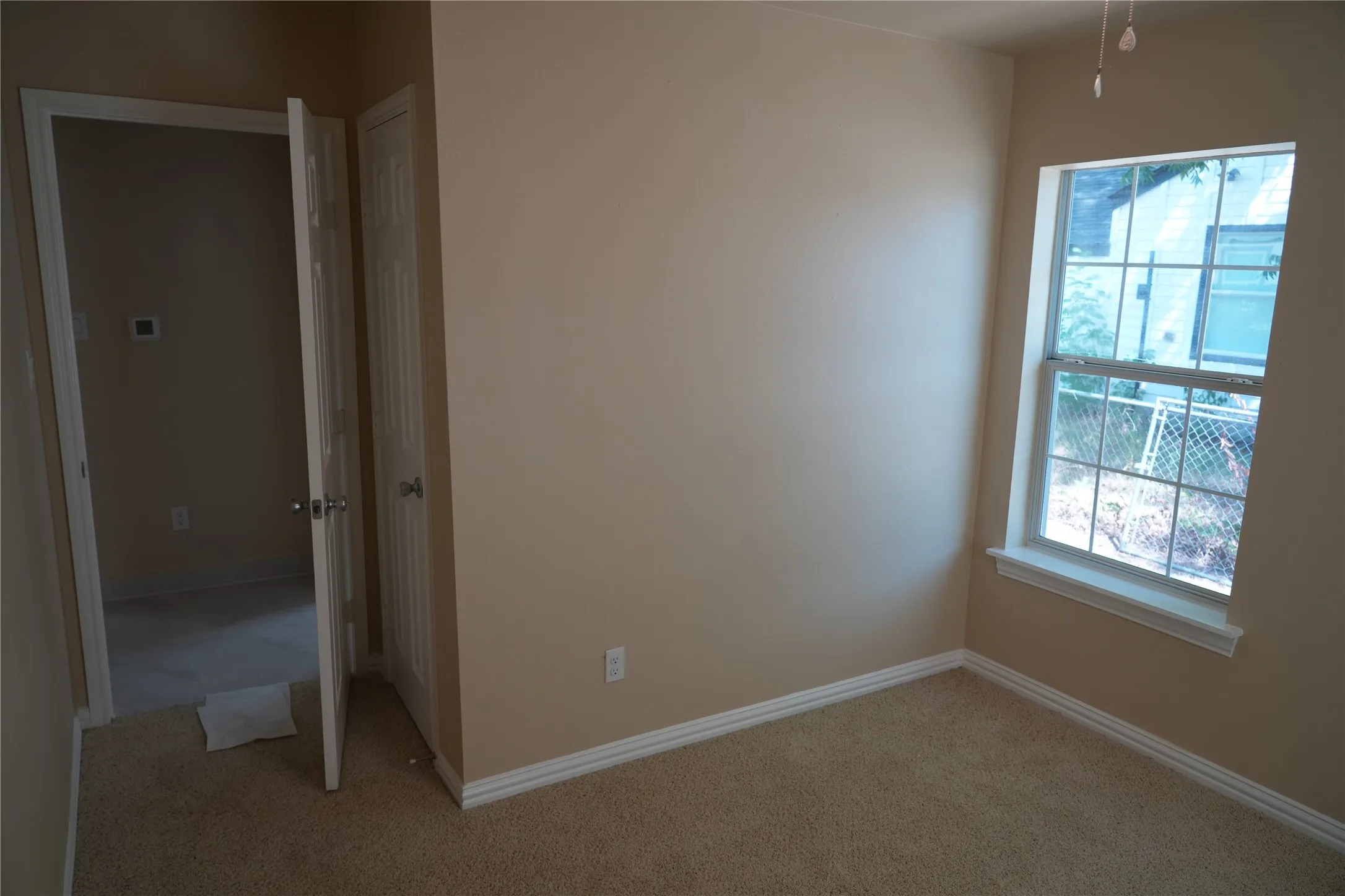 Neutral wall paint, carpet flooring, a multi-pane window with white trim, and a ceiling fan