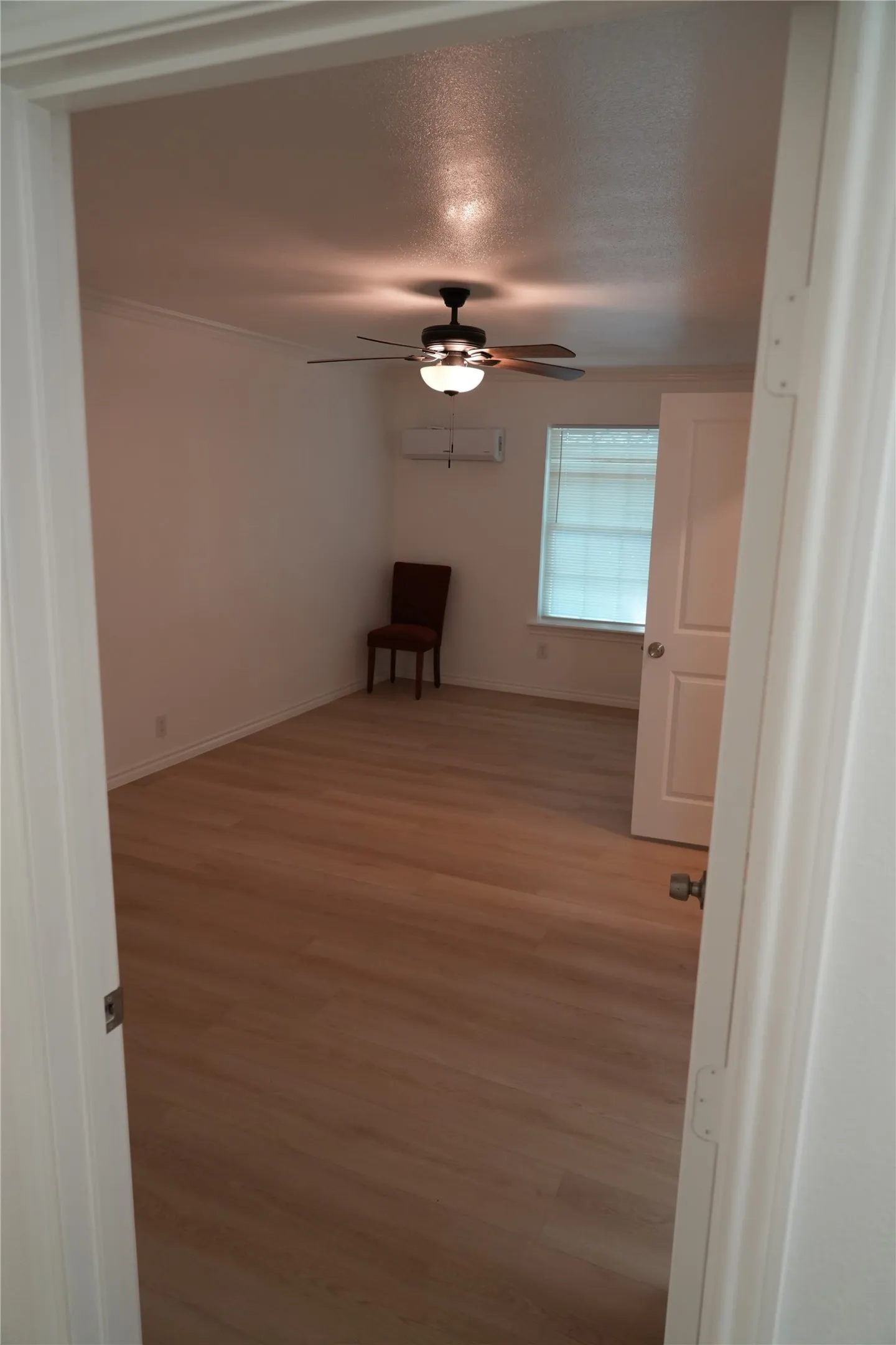 Spacious room featuring wood-finish flooring throughout, ceiling fan with integrated lighting, and large window allowing natural light