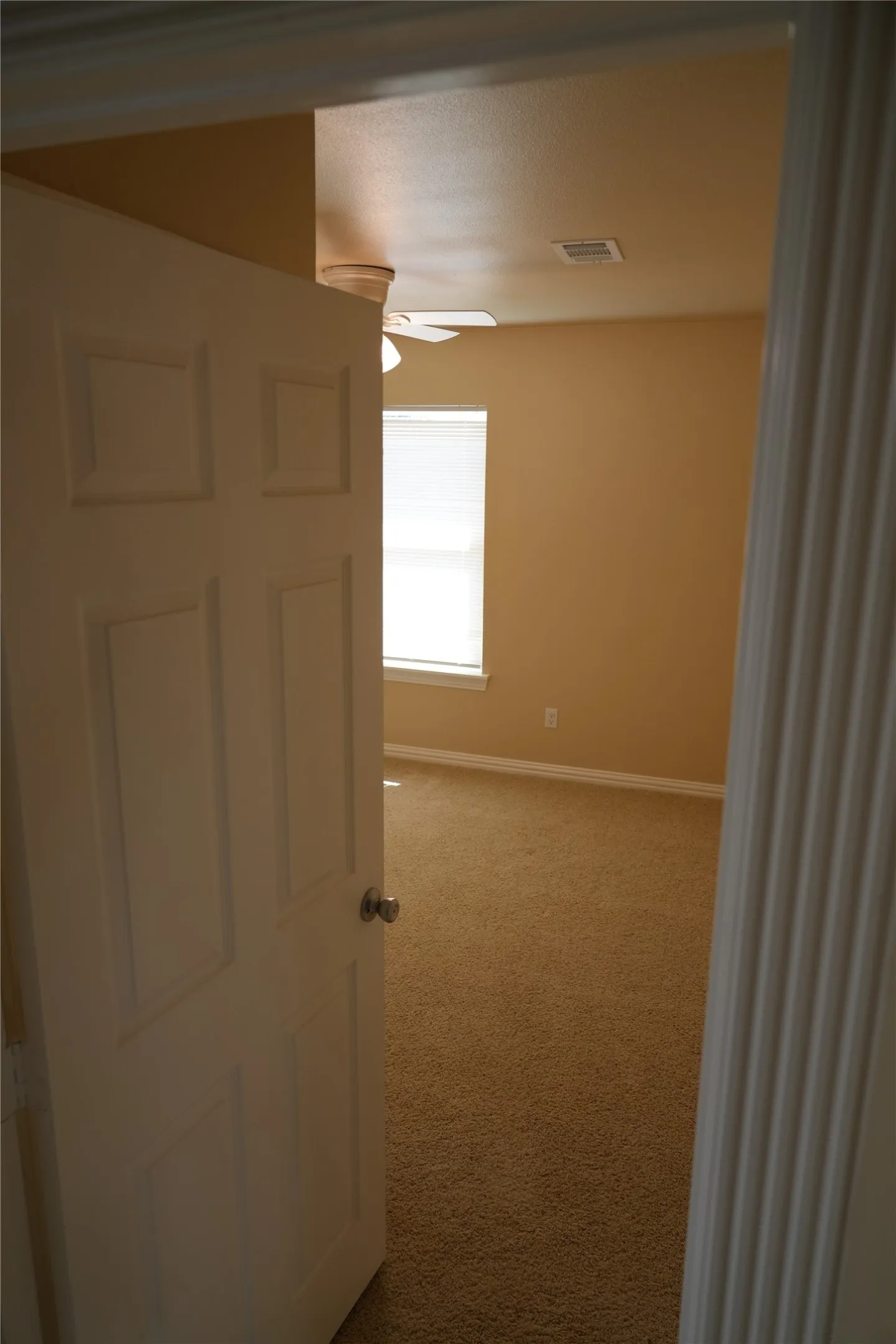 Neutral-toned wall finish, textured carpet flooring, window with blinds, and ceiling fan