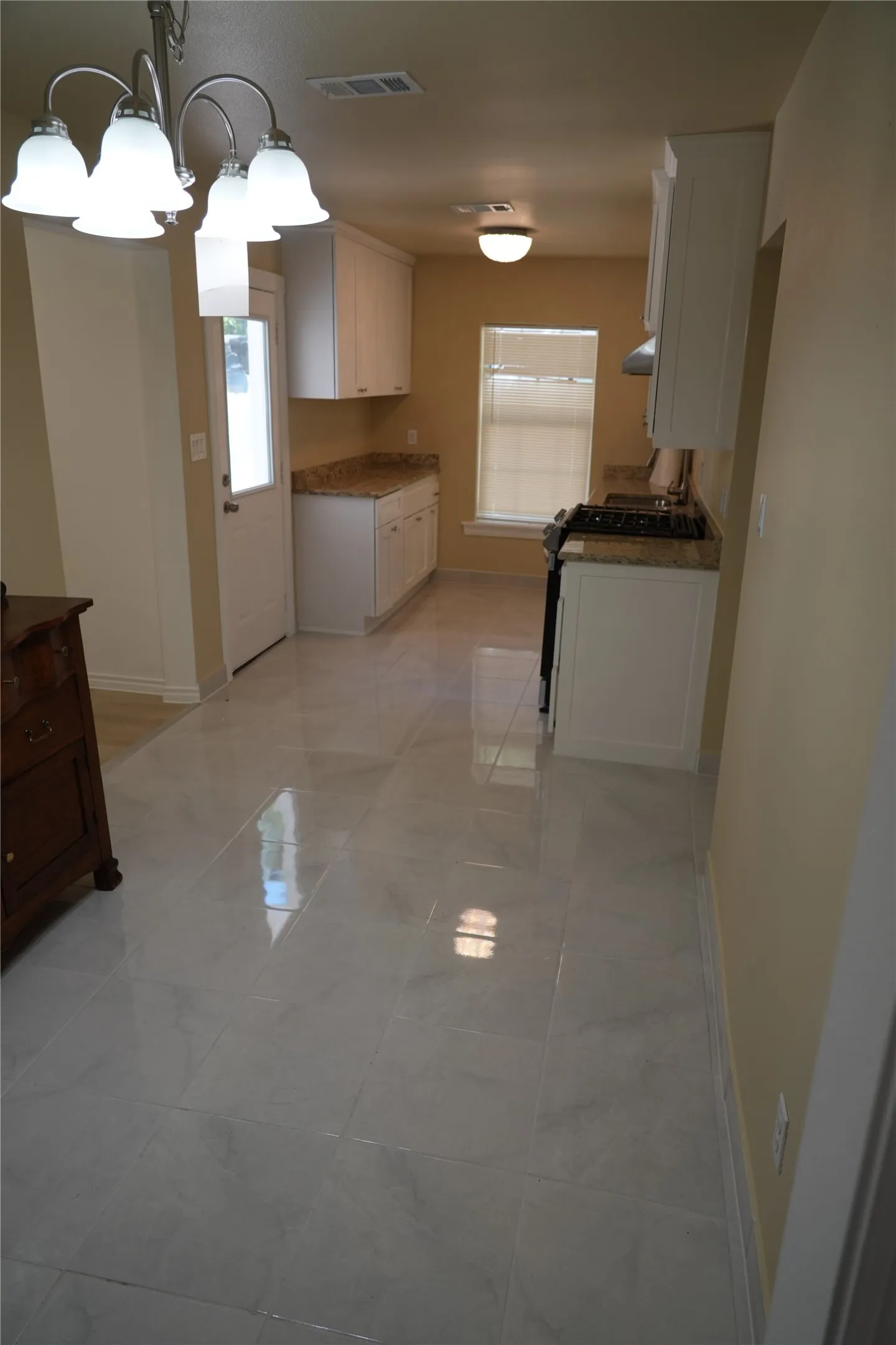 Kitchen featuring light-toned tile flooring, white cabinetry, speckled countertops, and a built-in range with a coordinating hood vent