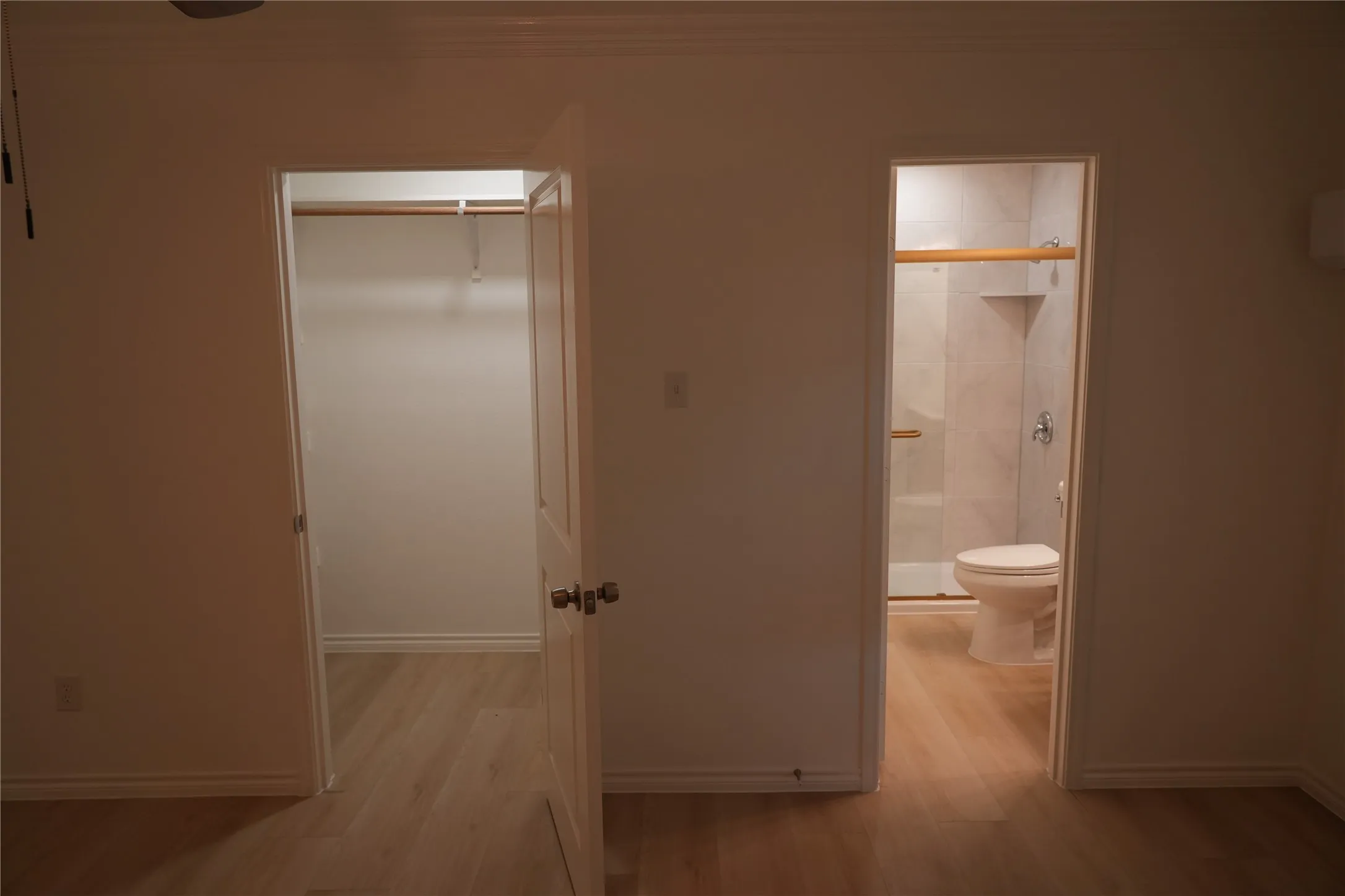 Wood-finish flooring throughout, with a built-in closet featuring hanging rods and a bathroom with a glass-enclosed shower and tiled walls