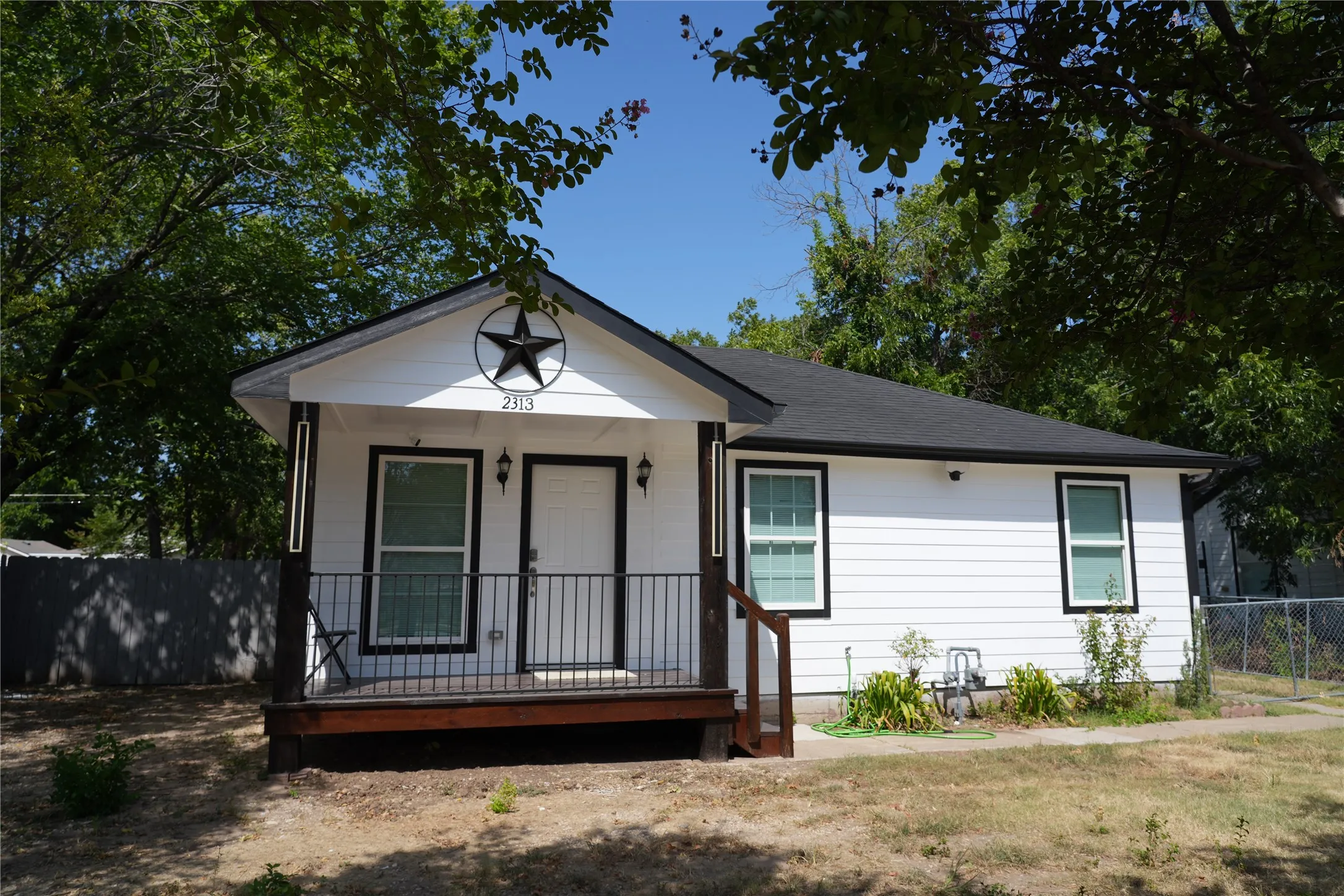 White exterior siding with dark trim windows, covered front porch with dark railing, dark roof, and a decorative star accent on the front gable
