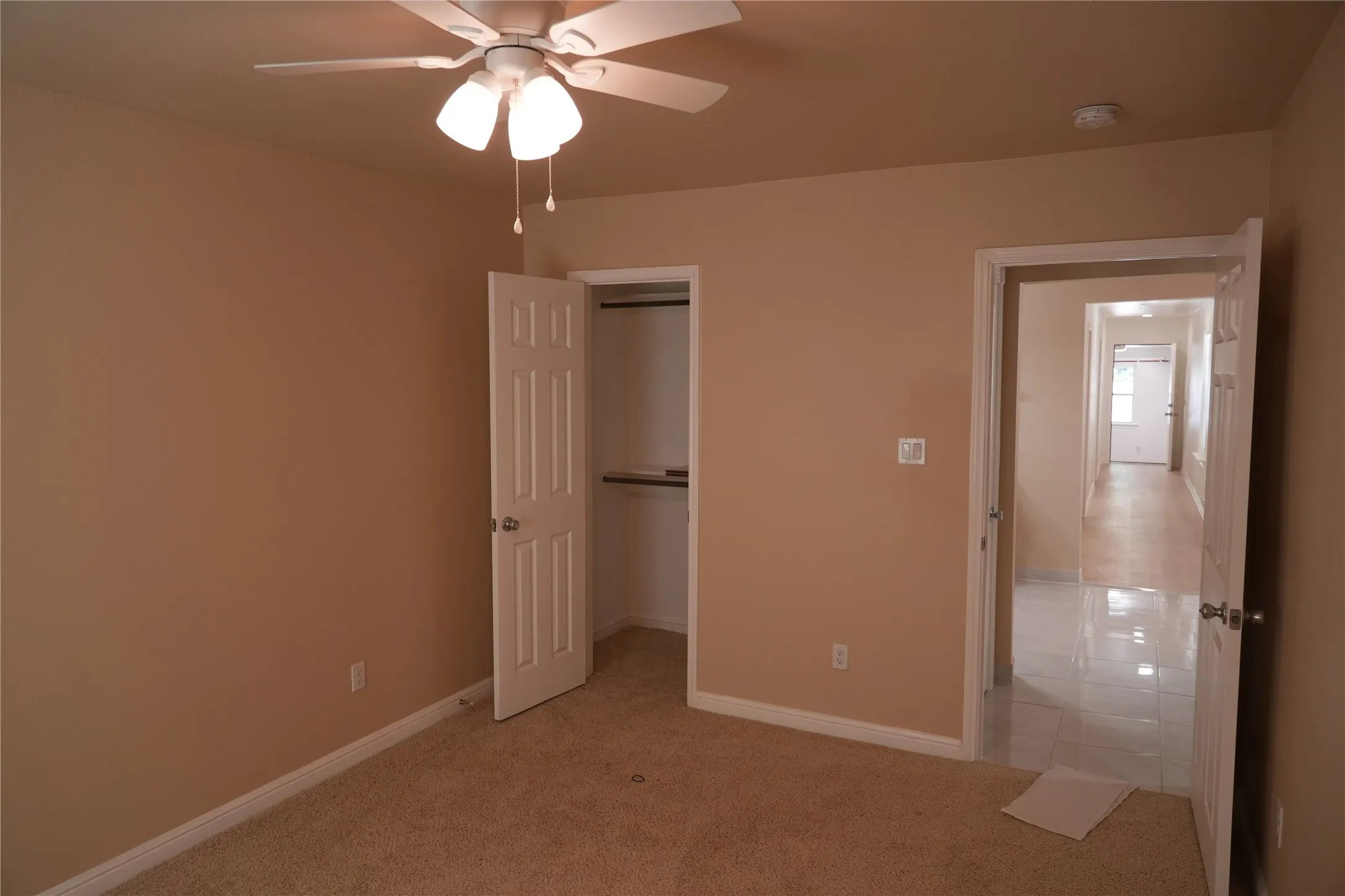 Carpeted room featuring a ceiling fan with integrated lighting, a built-in closet with shelving and hanging rod, and a doorway opening to a tiled hallway