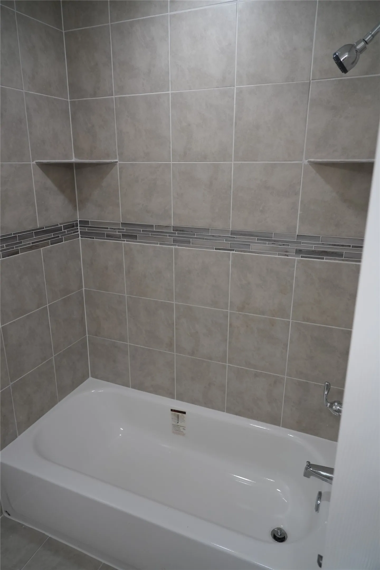 Subway tile shower surround with a decorative glass tile accent band, integrated corner shelves, and a chrome shower head and faucet