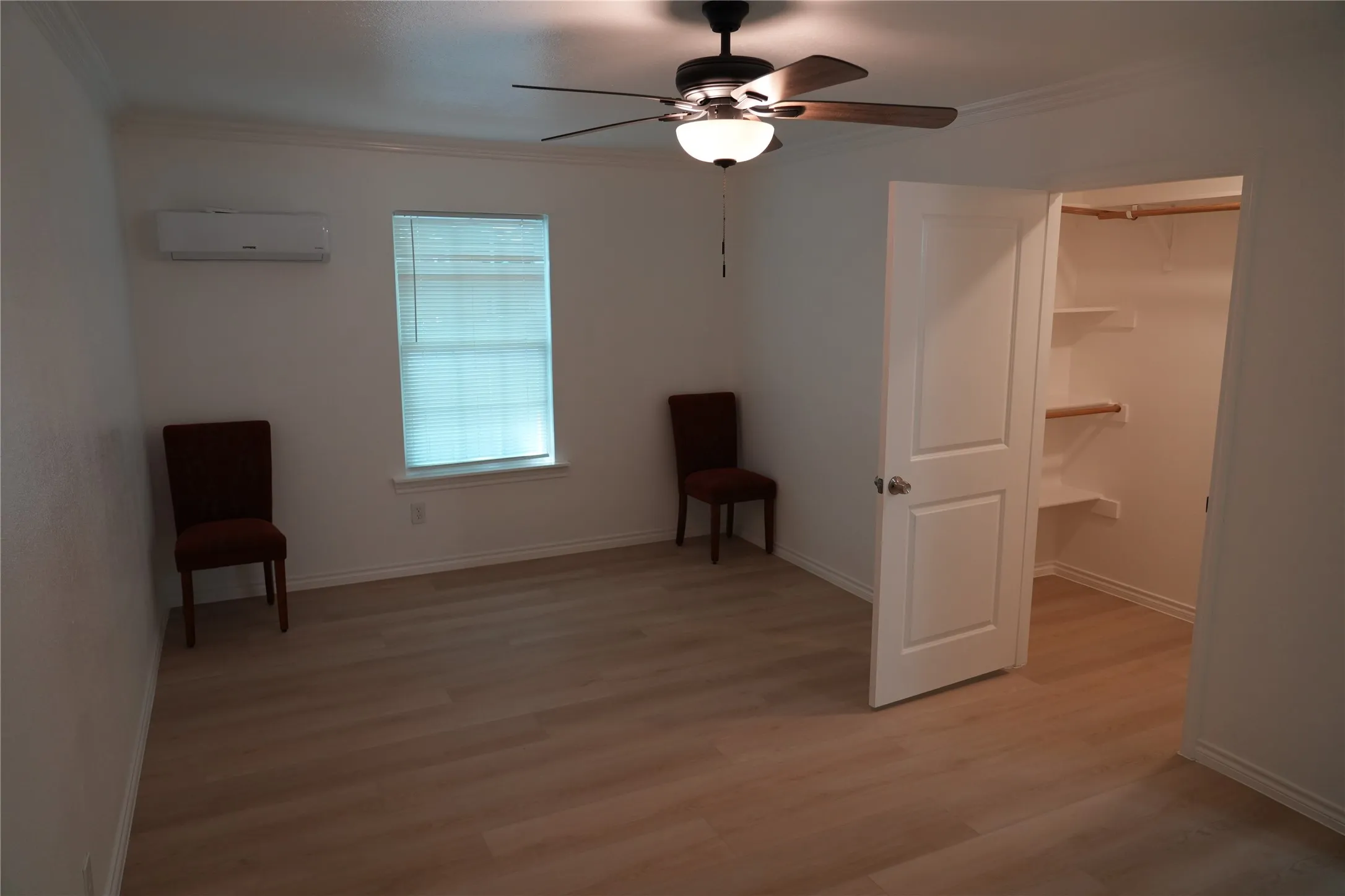Spacious room featuring wood-finish flooring, a ceiling fan, window with blinds, and a built-in closet with shelving and hanging rod