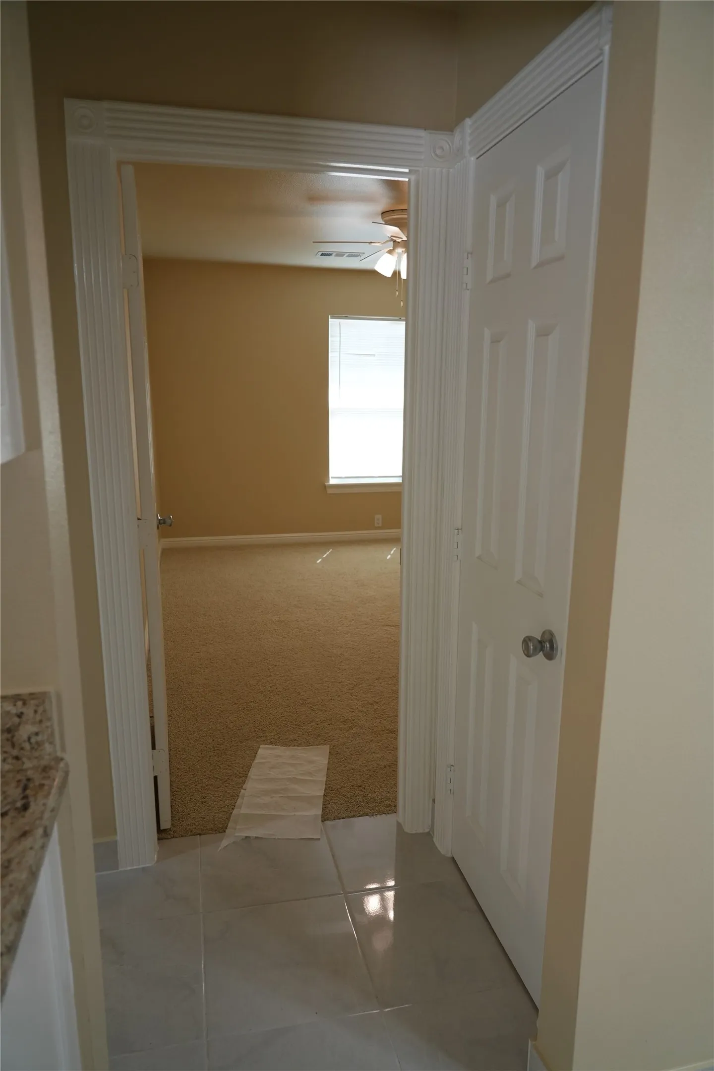 Porcelain tile flooring, decorative door frame, paneled interior door, carpeted room, ceiling fan