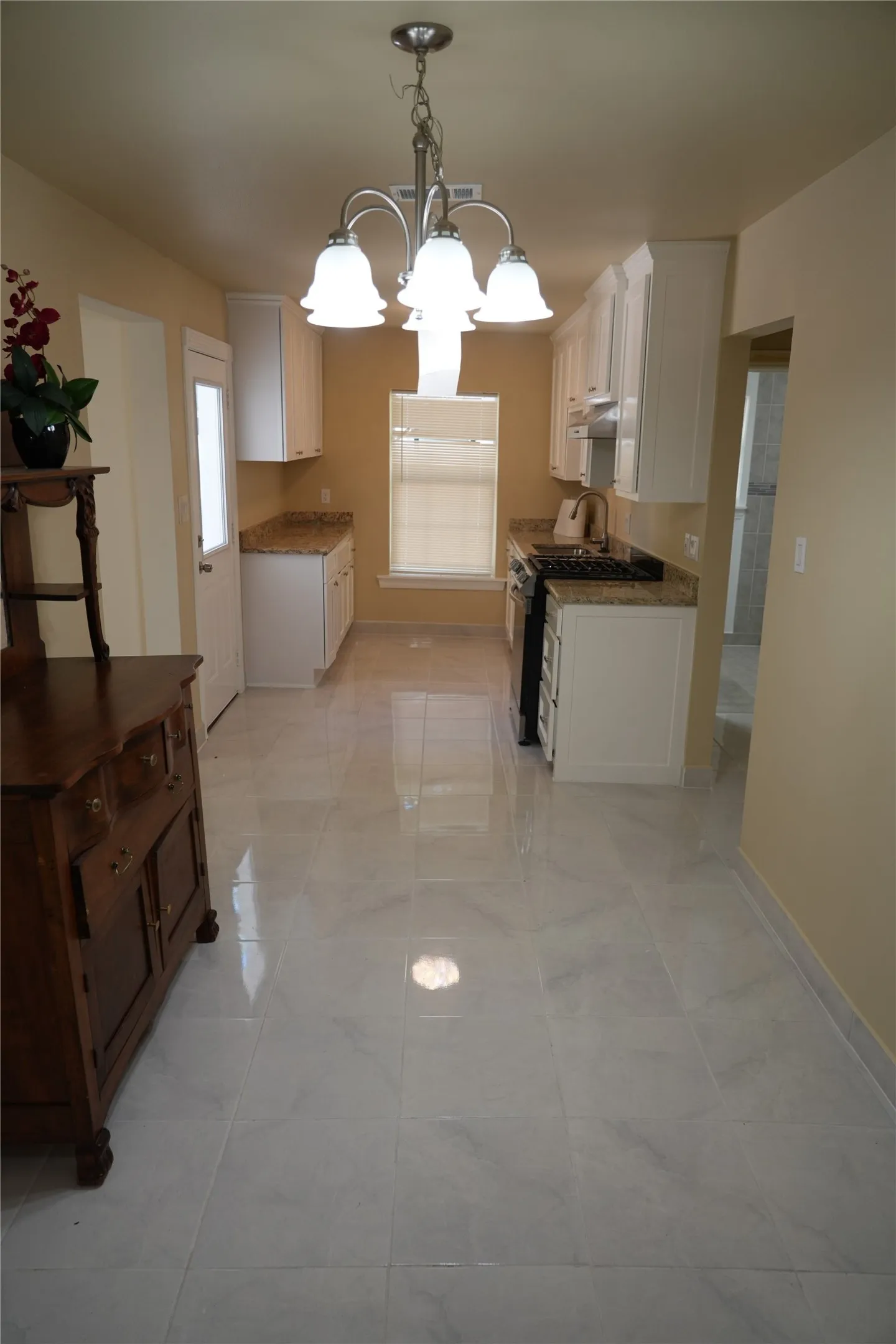 Galley kitchen featuring white cabinetry, stone-finish countertops, a gas range, and tile flooring