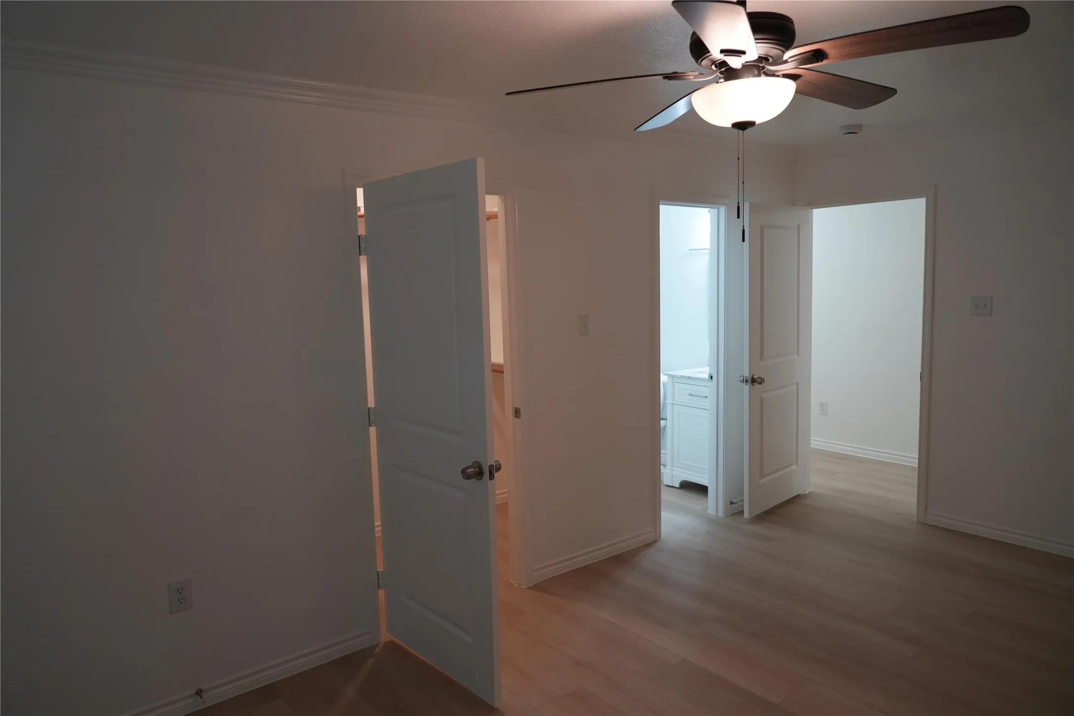 Crown molding, wood-finish flooring, ceiling fan with light fixture, paneled interior doors, and a bathroom vanity with sink