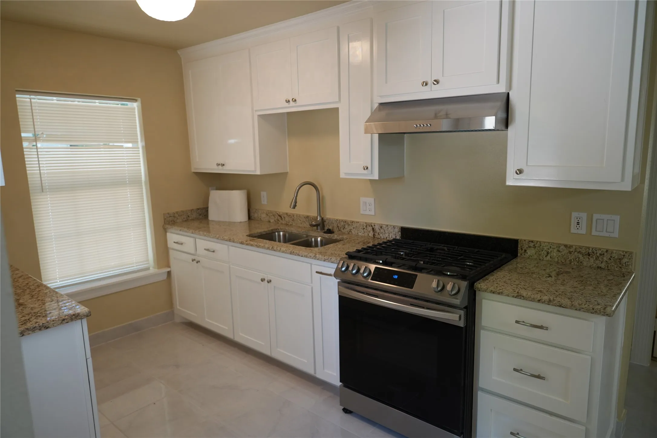 Kitchen featuring white cabinetry, light-toned stone countertops, a stainless steel gas range, a stainless steel range hood, and tile flooring