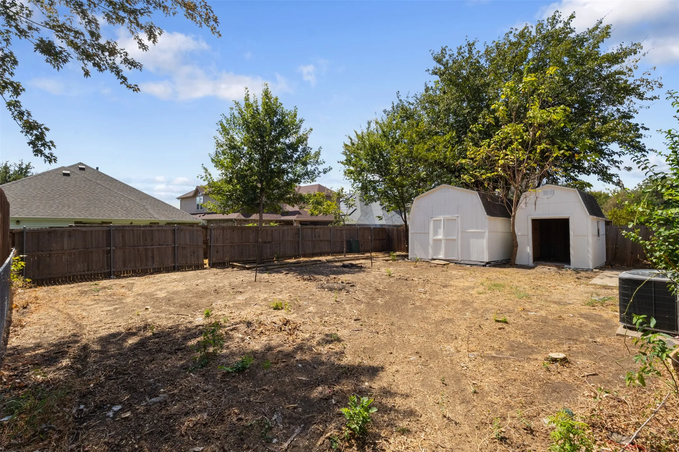 Expansive backyard with a wooden privacy fence, two storage sheds, and mature trees