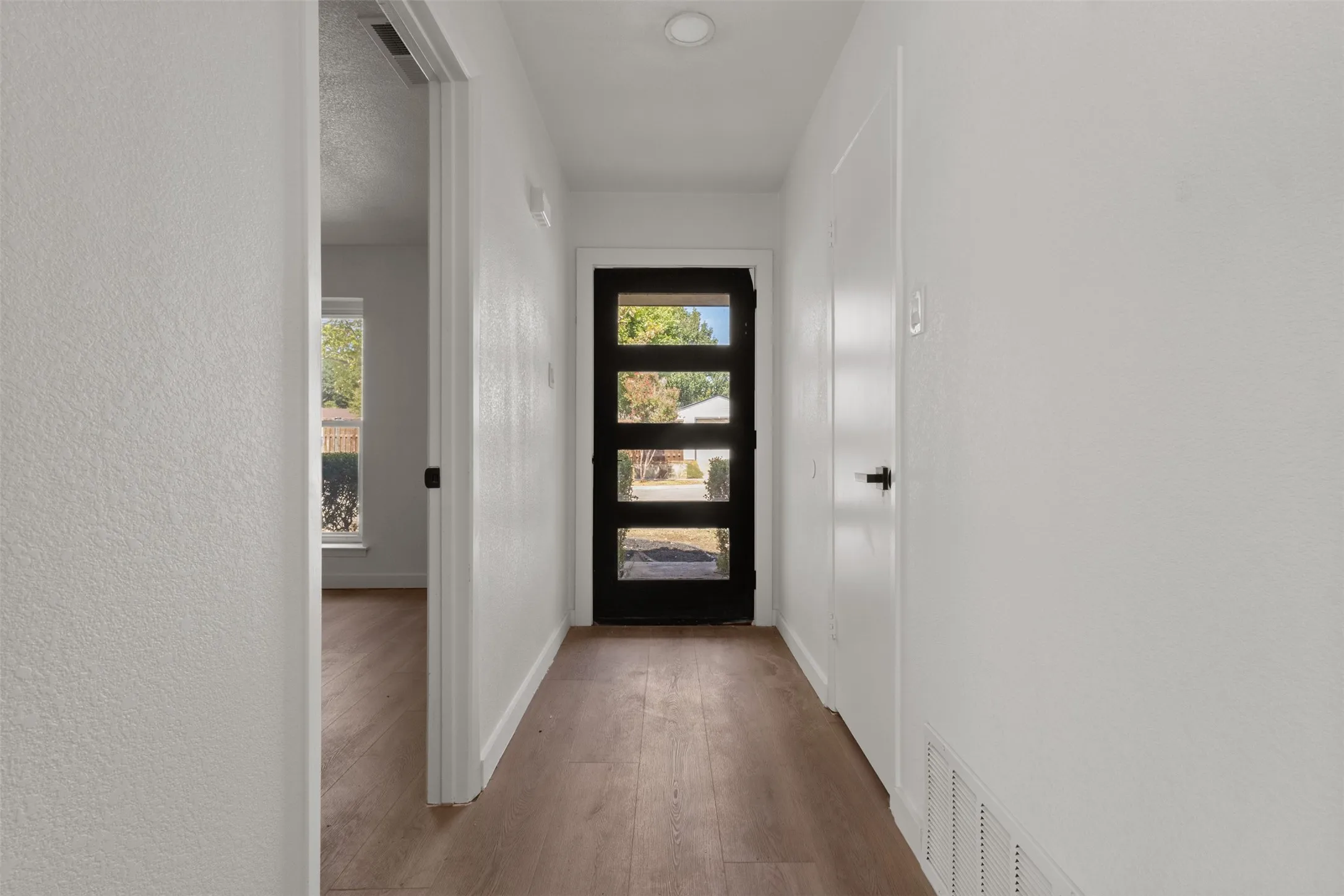 Entryway featuring wood-finish flooring and a modern dark-framed door with vertical lites