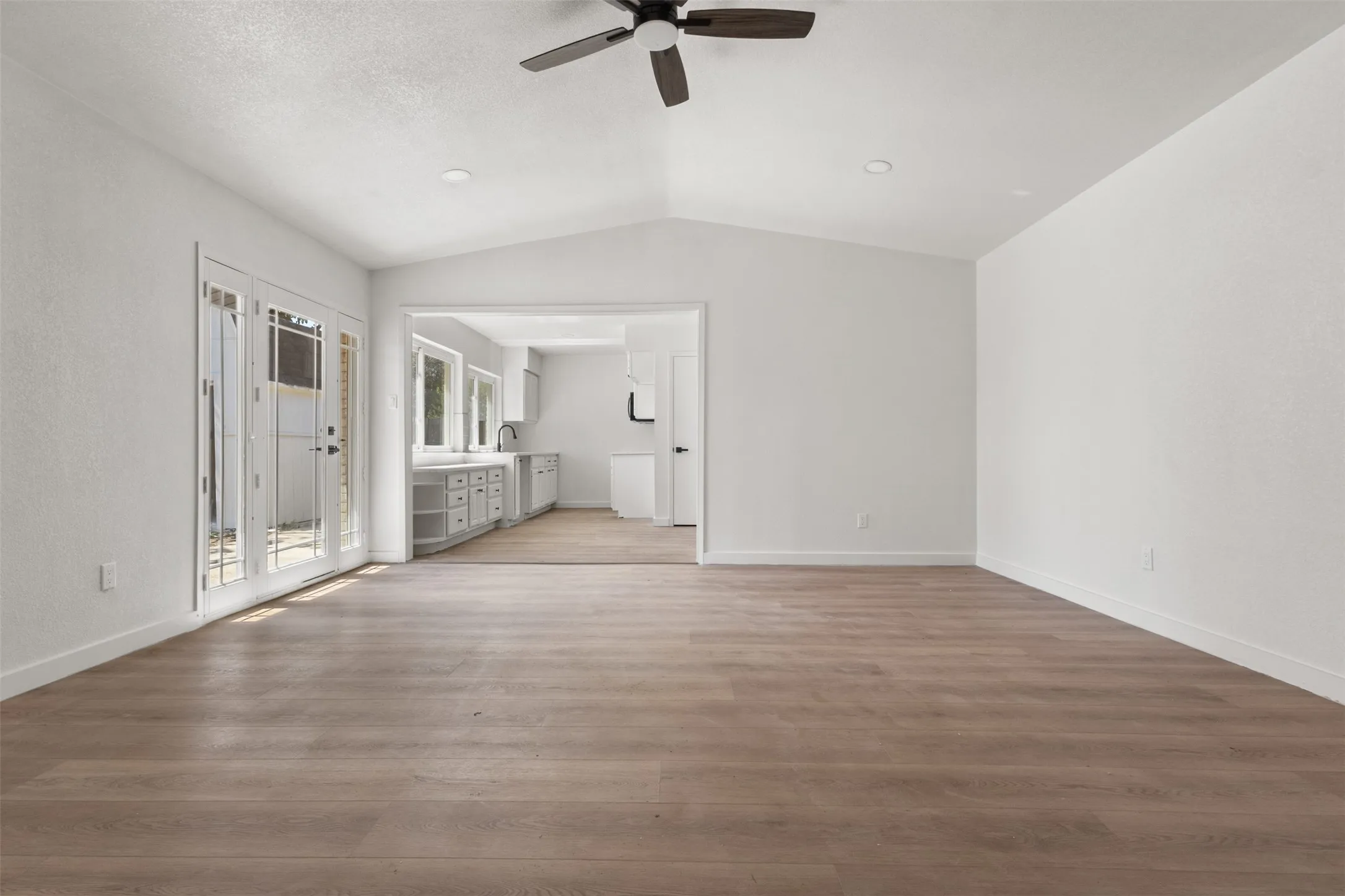Vaulted ceiling with a ceiling fan, wood-finish flooring, recessed lighting, double glass-panel doors, and an open concept layout