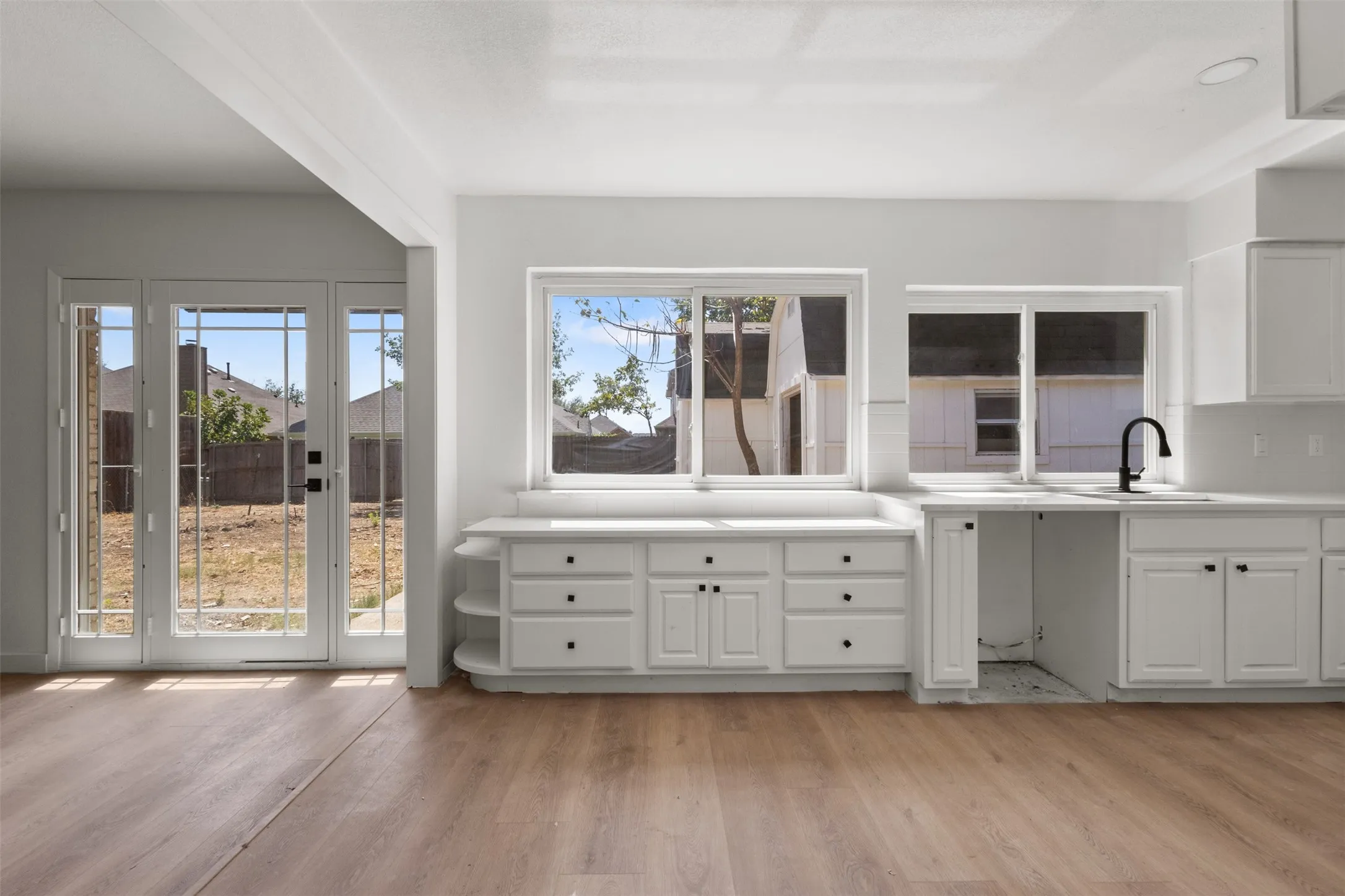 Wood-finish flooring throughout, white cabinetry with black hardware, white countertops, two large windows, and French doors