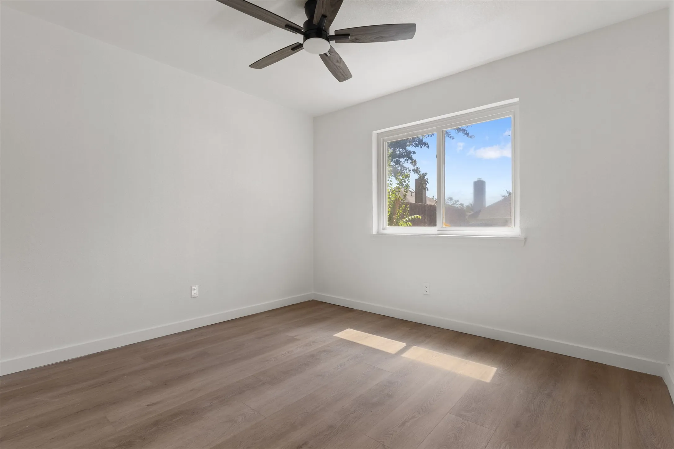 Wood-finish flooring, white walls, white trim, recessed window, and a ceiling fan with light fixture