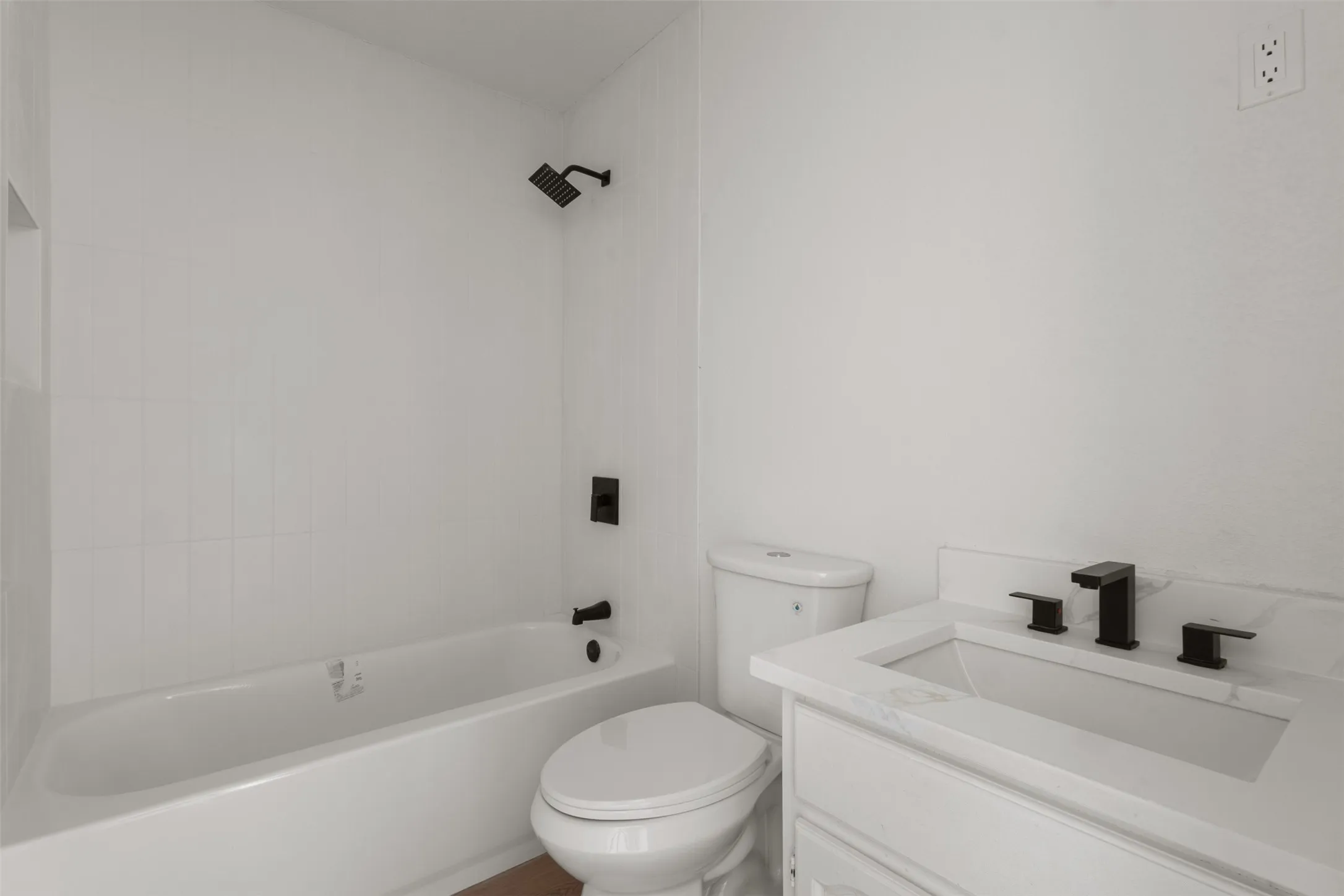 White tiled tub/shower combination with matte black fixtures, white vanity with integrated sink, and white countertop