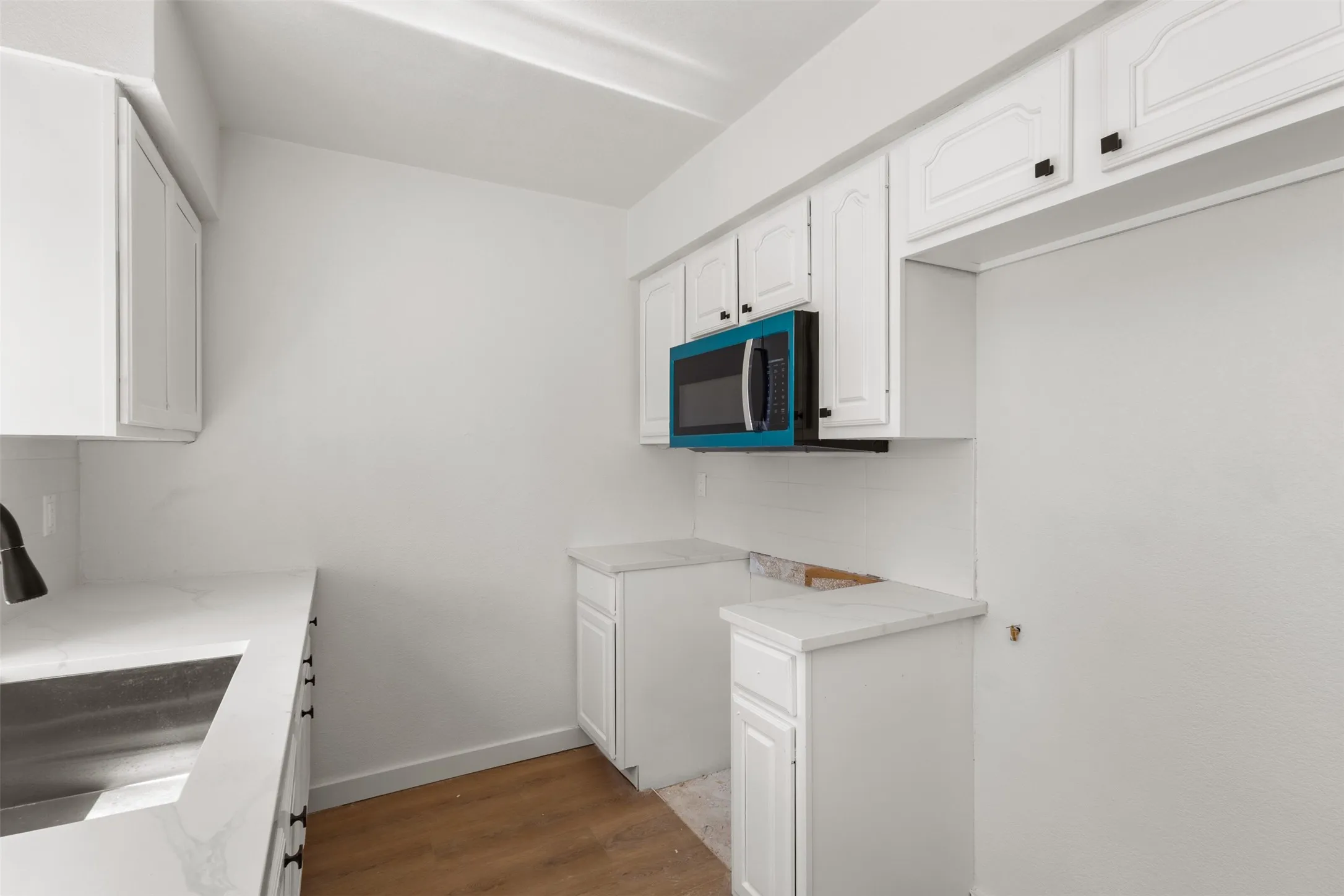 White cabinetry with black hardware, wood-finish flooring, undermount stainless steel sink, white countertops, and an over-range microwave